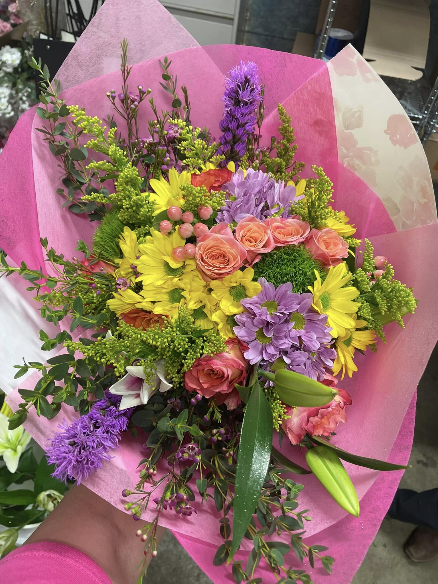 Mixed bouquet of pink roses, yellow daisies, and purple flowers wrapped in pink paper