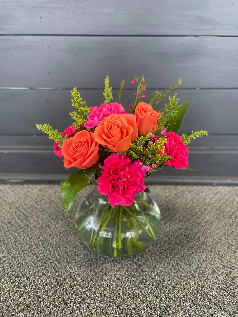 Orange roses and hot pink carnations in a clear glass vase
