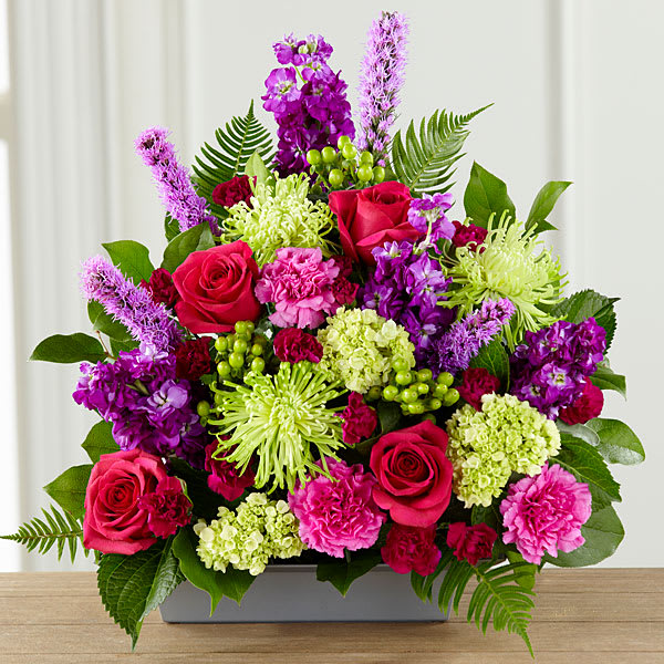 Bright mixed bouquet with roses, carnations, and purple blooms in a rectangular vase