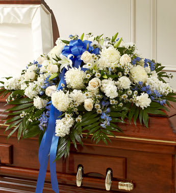 White floral casket spray with blue ribbon on a wooden coffin