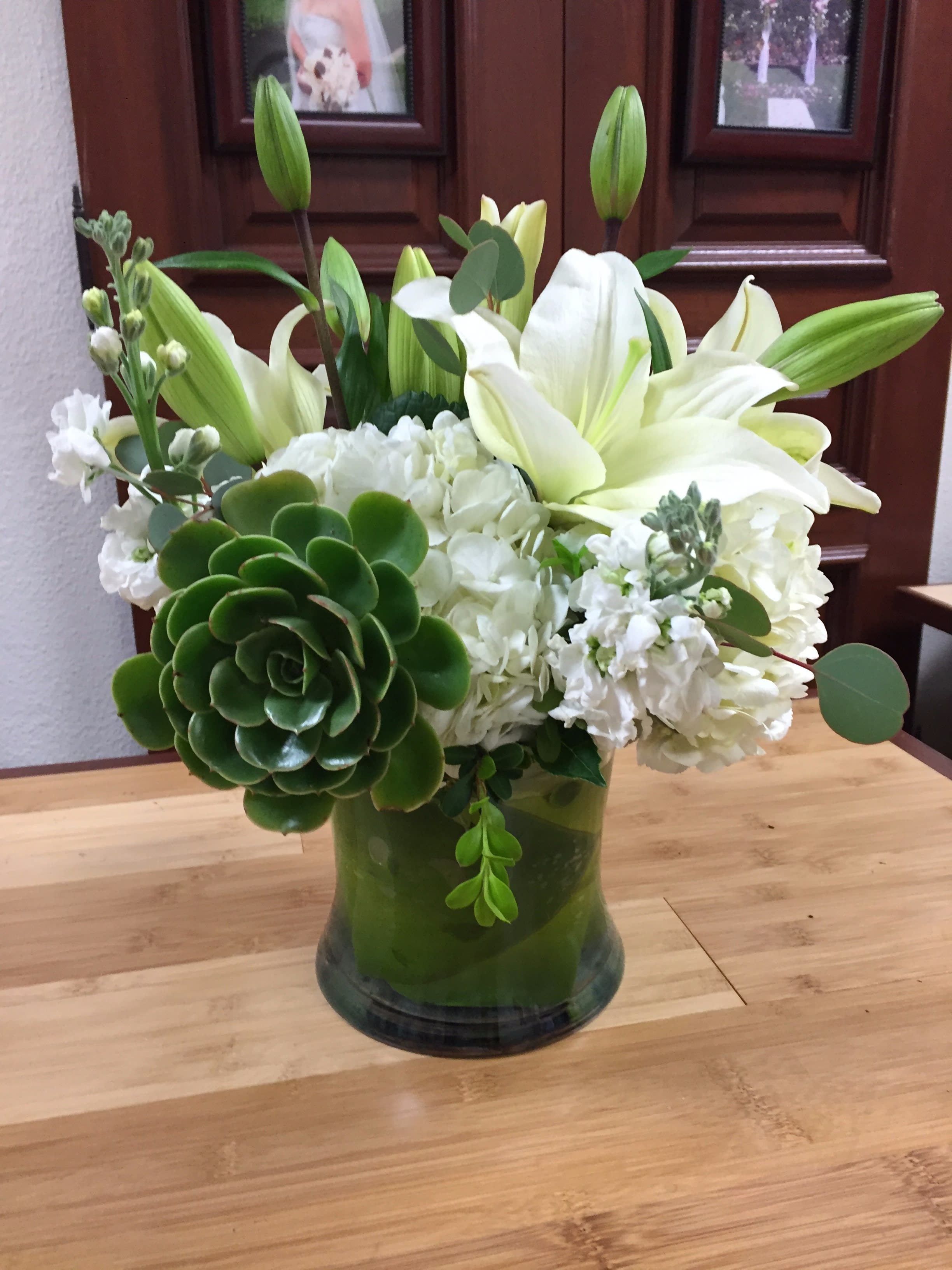 White lilies and hydrangeas in a green glass vase with succulents.