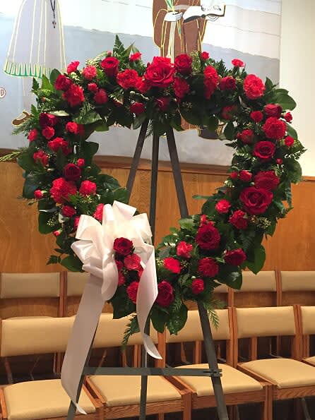 Heart-shaped red rose wreath on an easel with a white ribbon bow