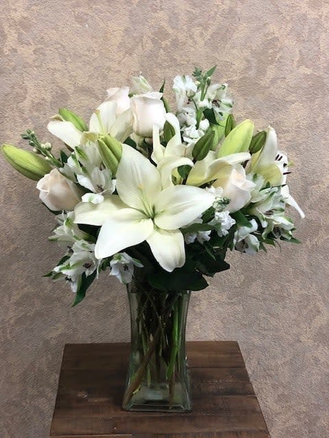 White lilies and roses arranged in a clear glass vase