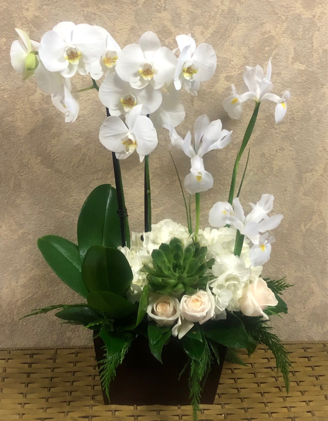 White orchids and pale roses arranged in a dark square container