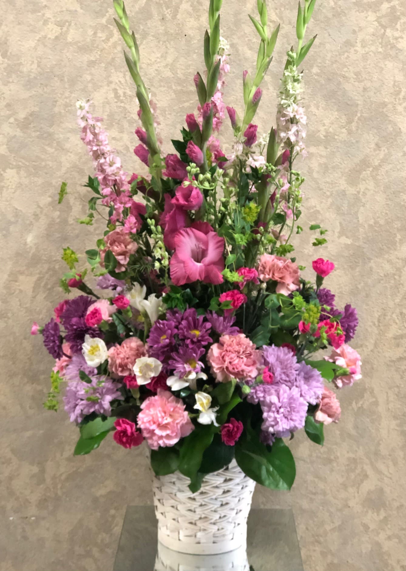 Tall pink and purple floral arrangement in a white woven basket