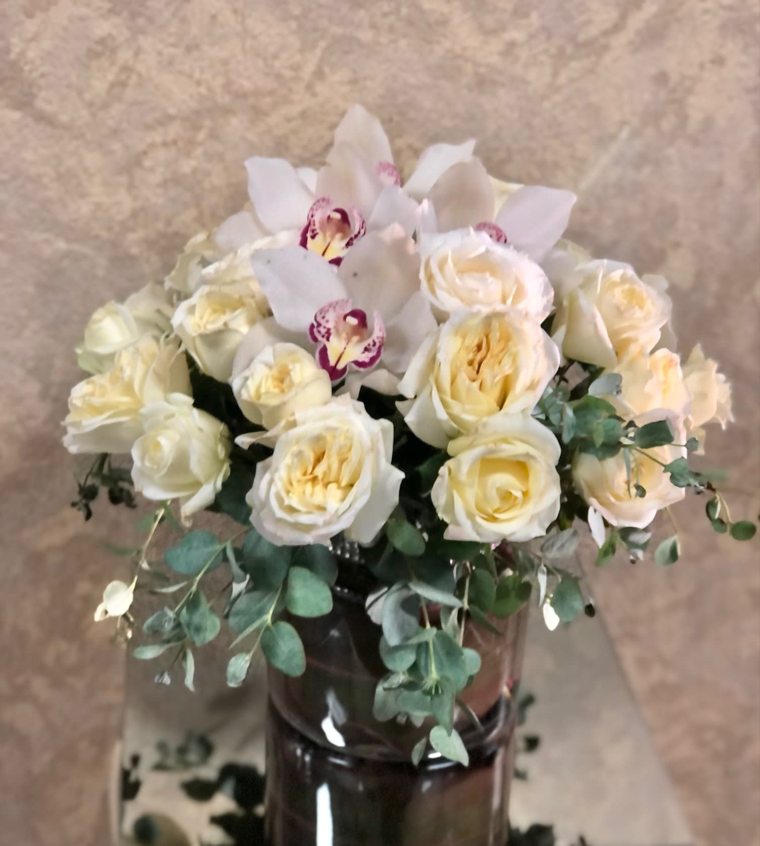 Cream roses and white orchids arranged in a dark glass vase
