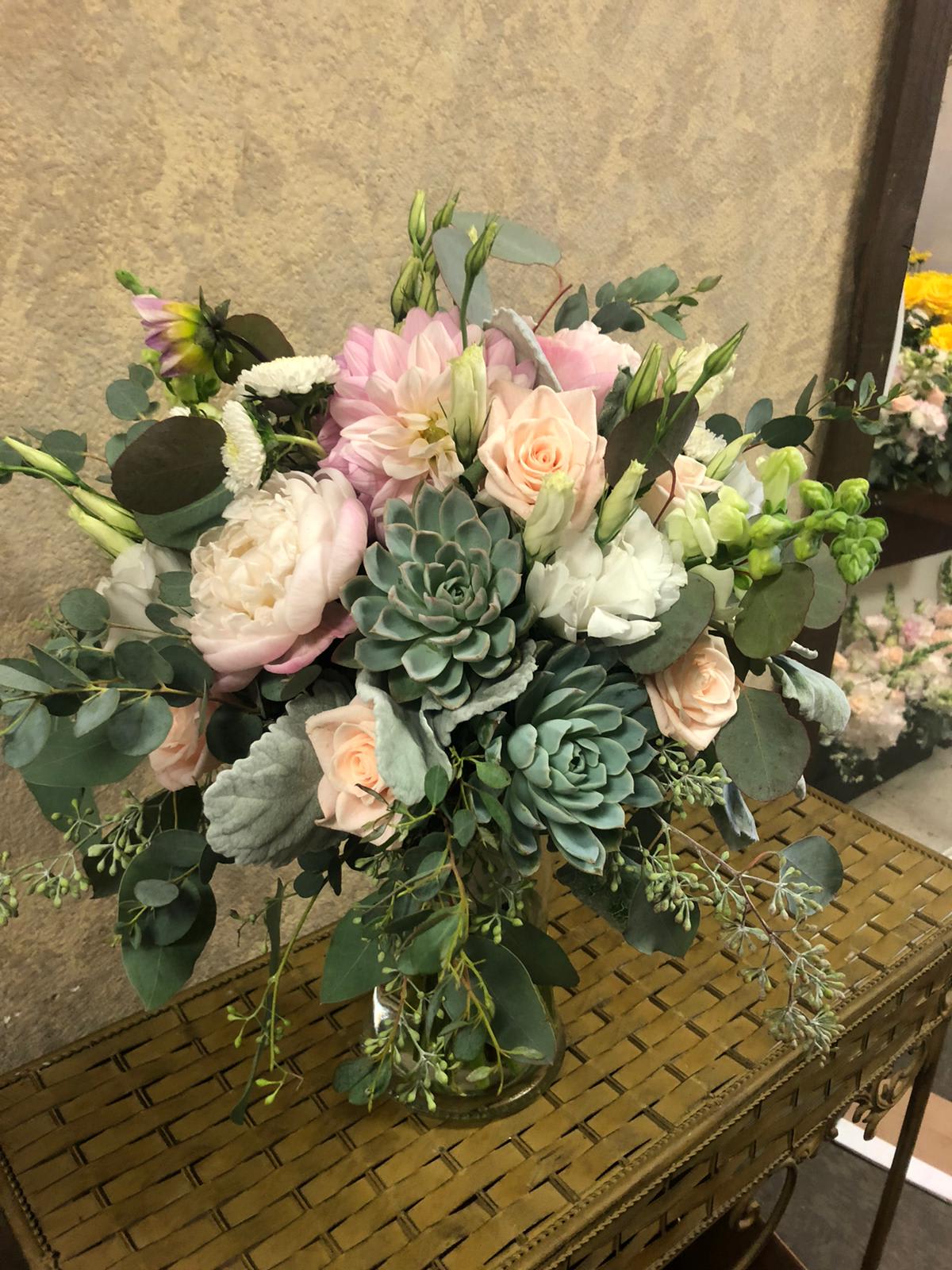 Bouquet of blush roses, pale pink blooms, and succulents in a glass vase