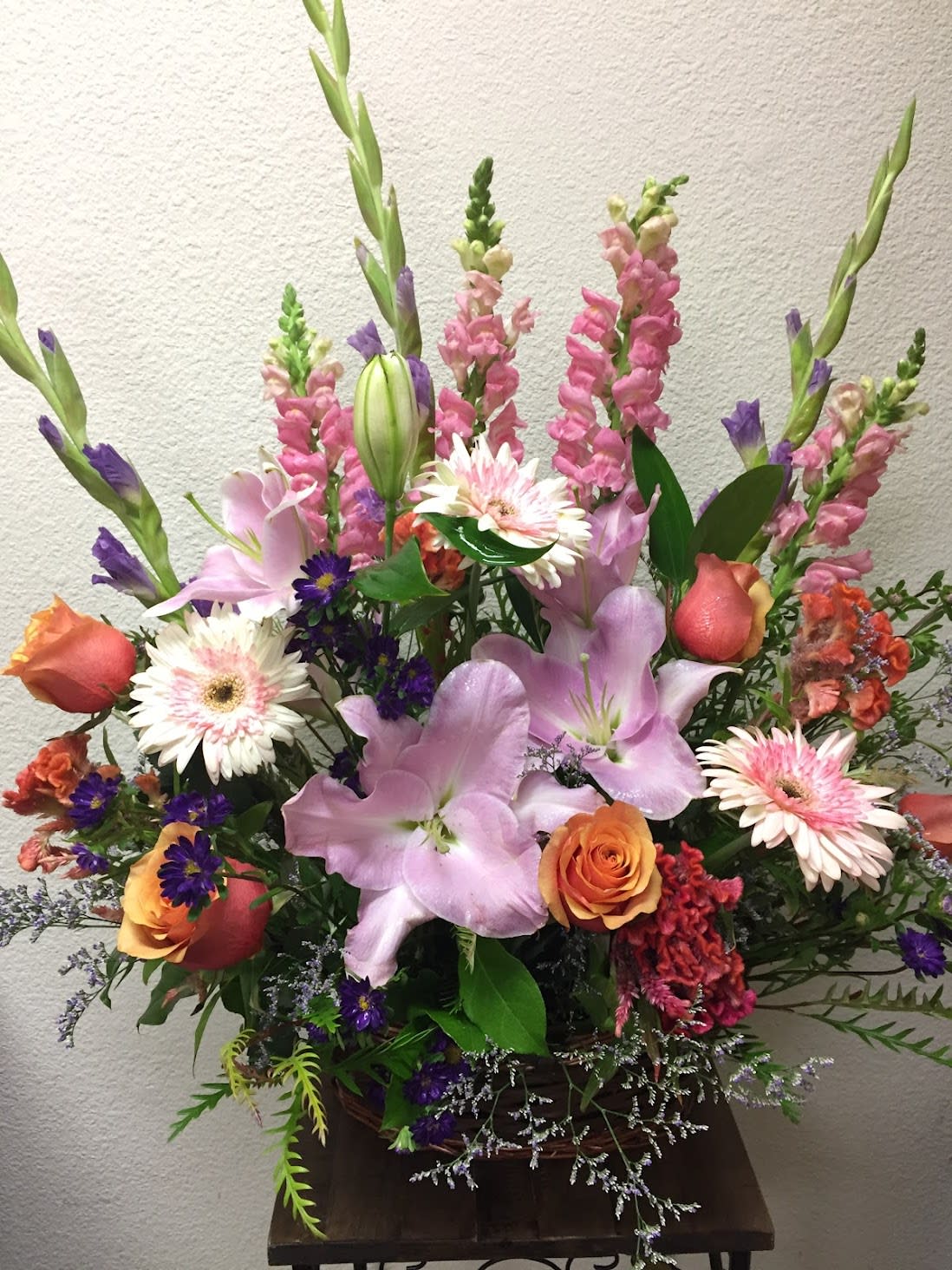 Mixed bouquet with pink lilies, roses, and tall snapdragons in a basket