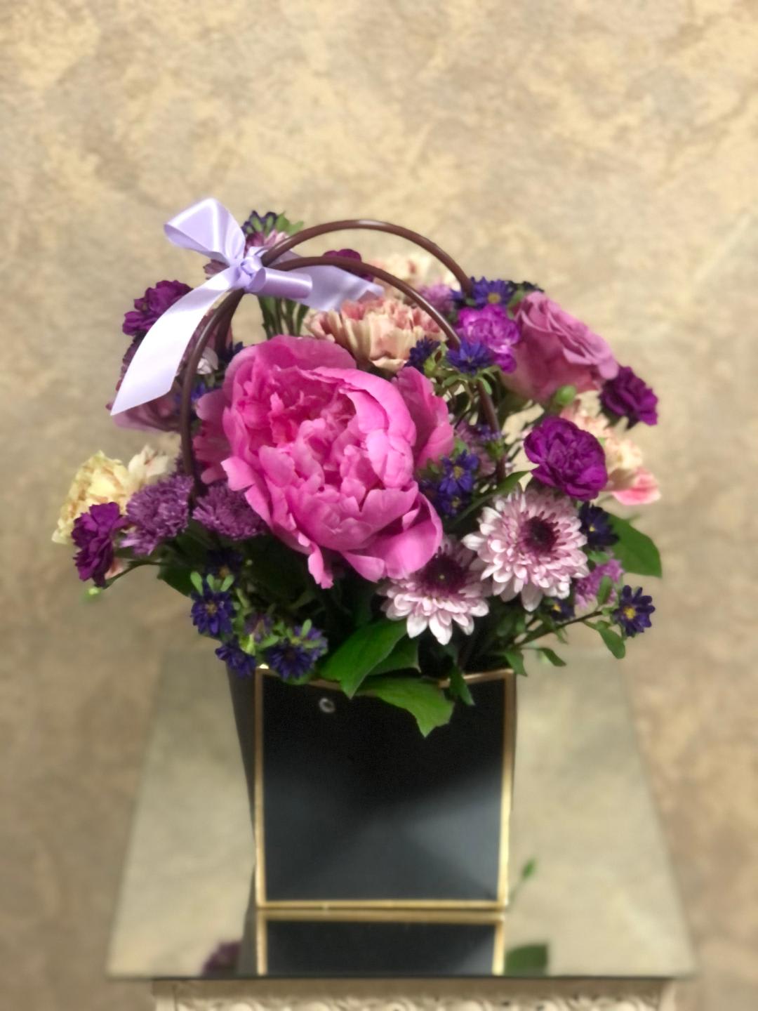 Pink and purple flower basket with a ribbon on a black box