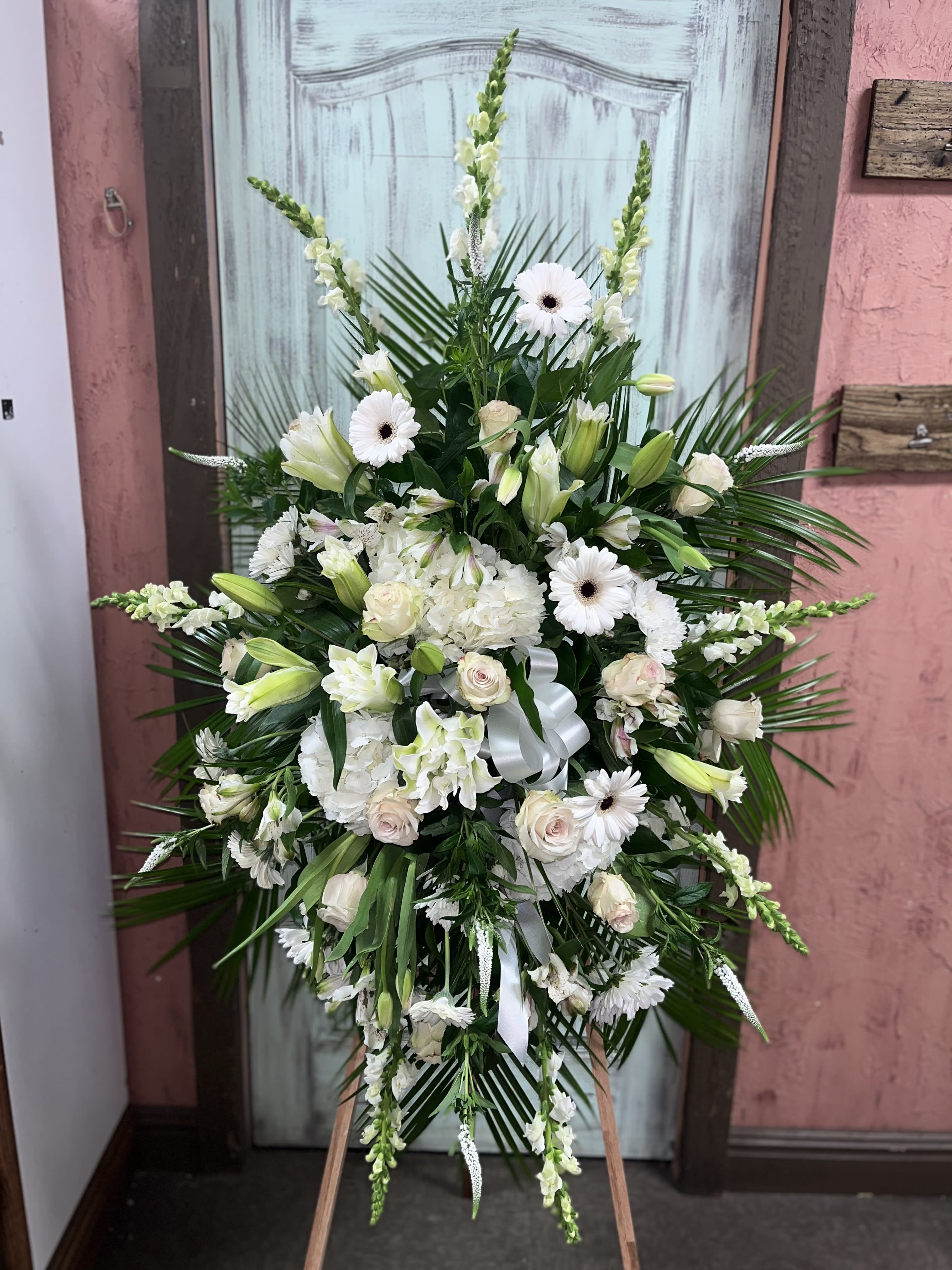 Large white funeral spray with lilies, roses, and daisies on an easel