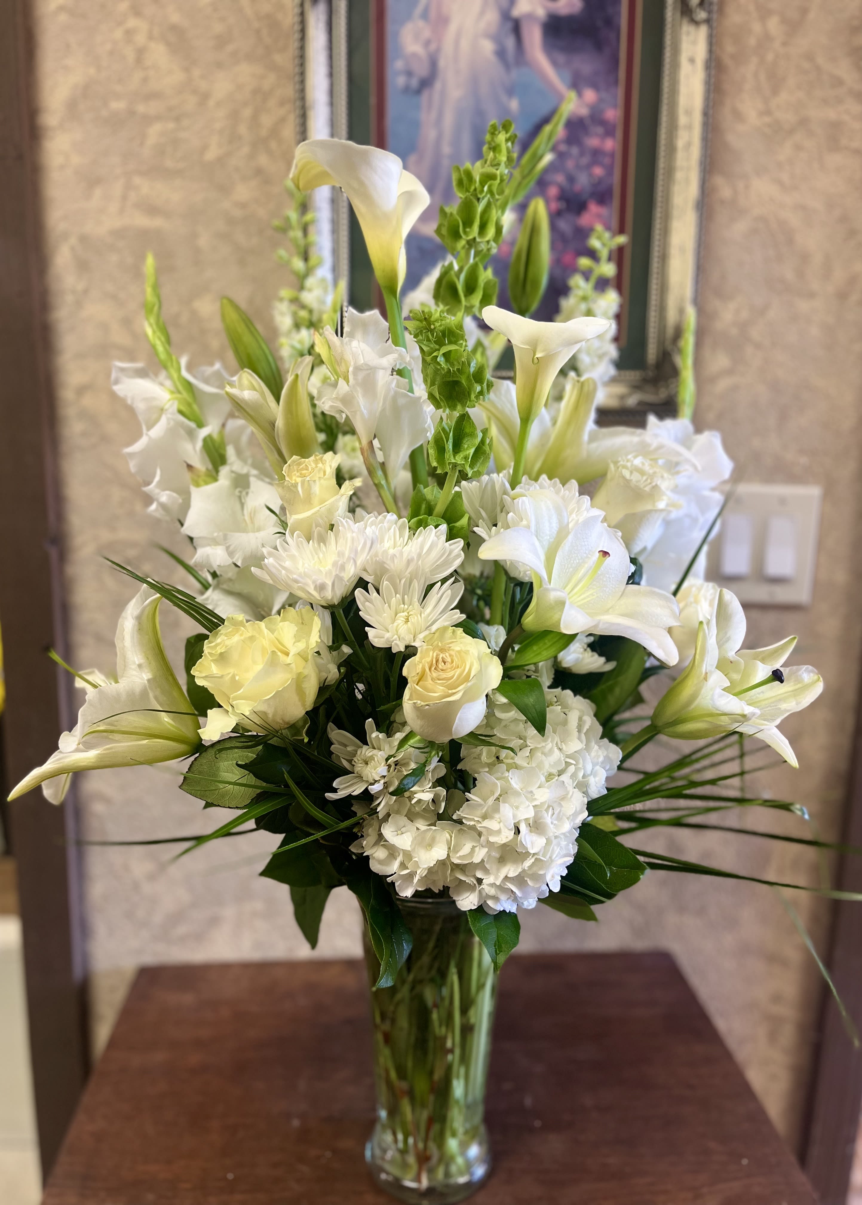 White floral arrangement in a clear glass vase with lilies, roses, and hydrangea