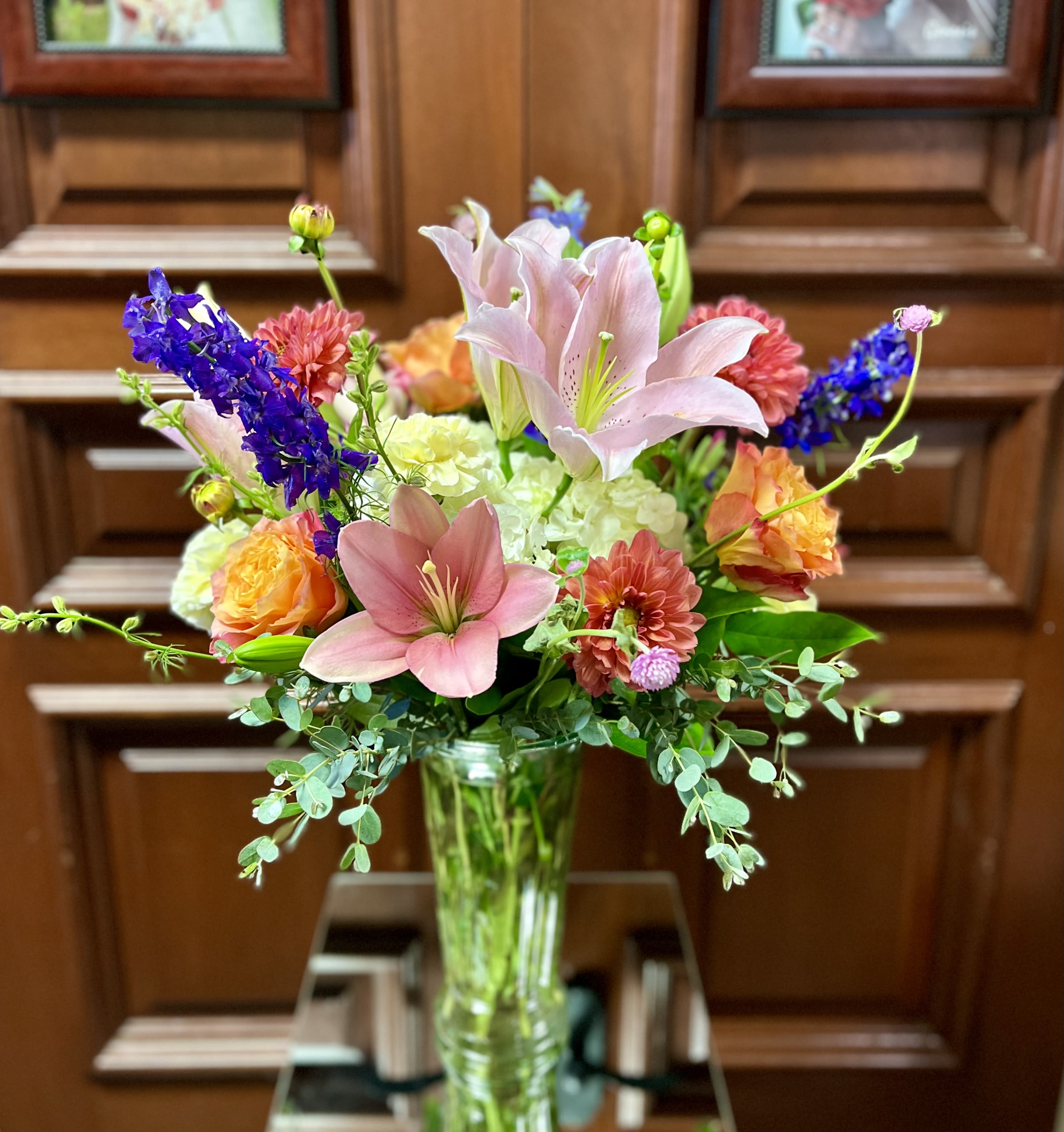 Cheerful Wishes - Recipe: Pink Asiatic Lilies, Purple Larkspur, Orange/Pink Seasonal Dahlias, White Hydrangaes, Orange Roses and greens in a tall clear vase.  Availability: Dahlias mid-sum-Autumn Design View: All Facing View Photo shown: Standard