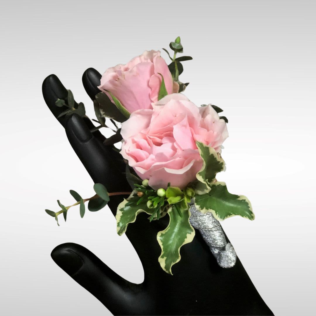 Small pink rose corsage with silver-wrapped stems displayed on a black mannequin hand