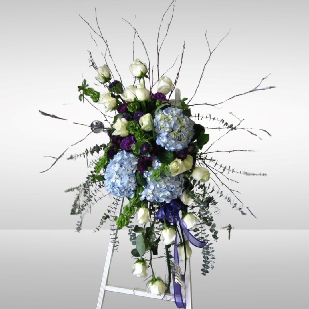 Tall floral spray with white roses, blue hydrangeas, and purple accents on an easel