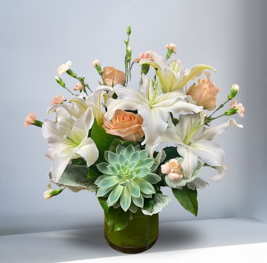 White lilies and peach roses in a green glass vase with a succulent accent