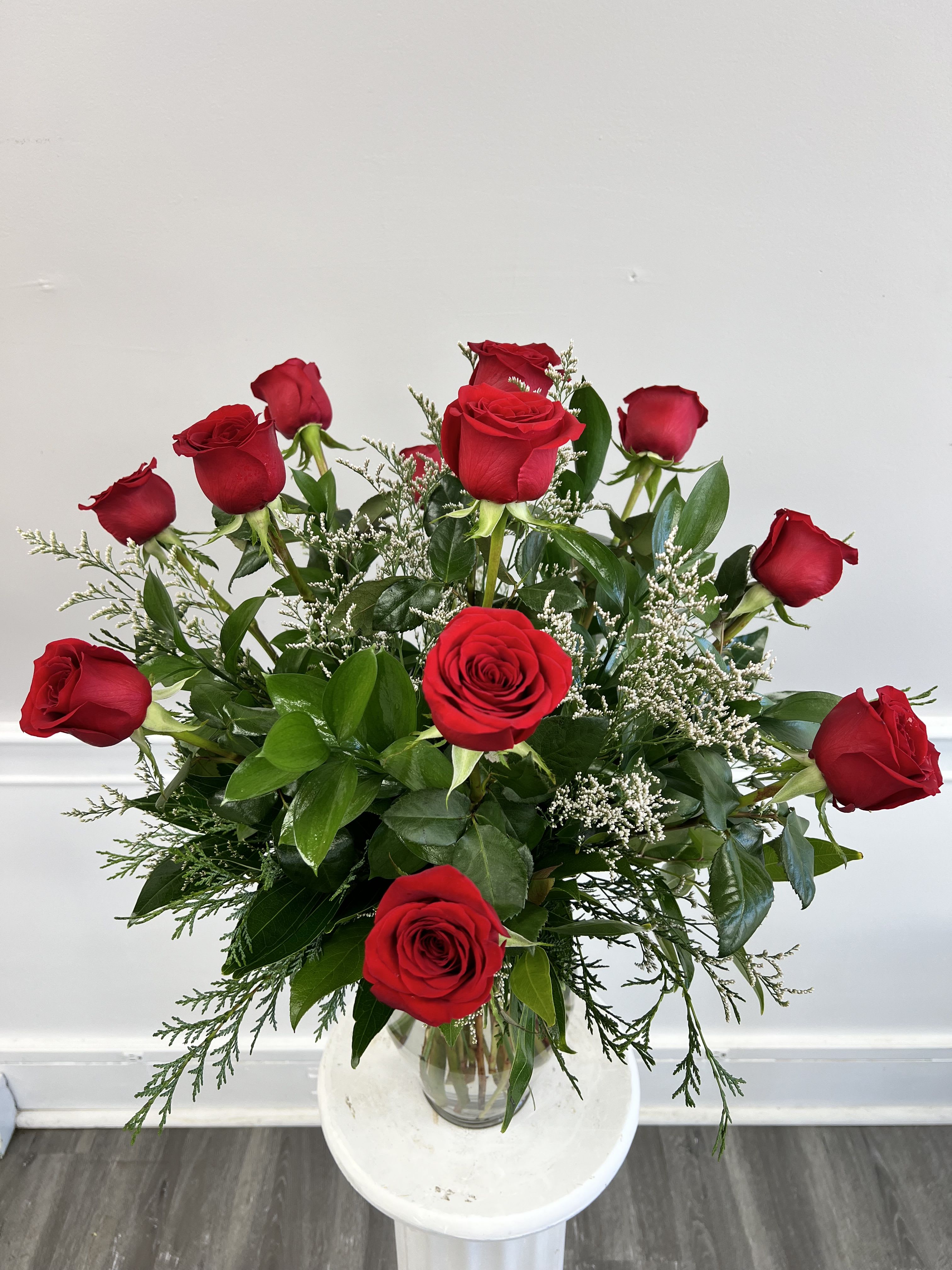 Arrangement of long-stem red roses with small white filler flowers in a clear glass vase