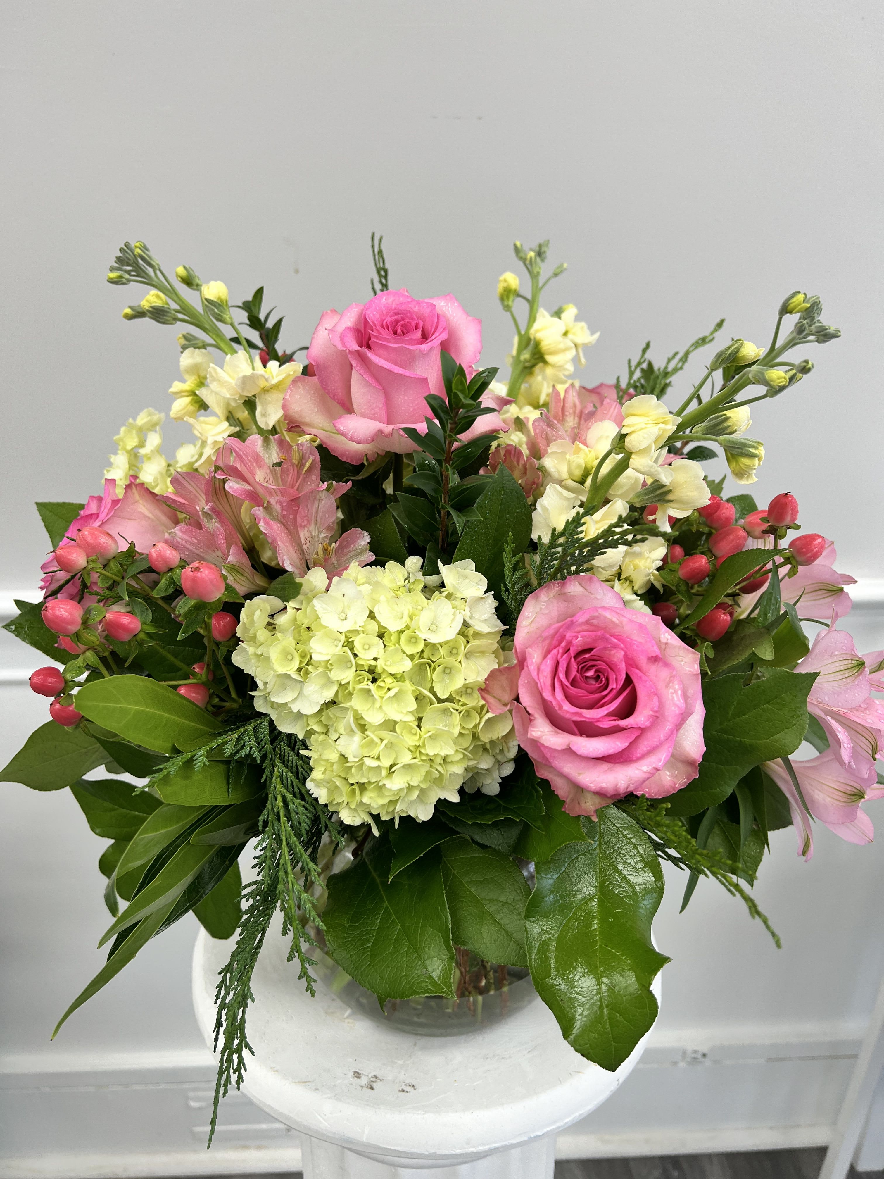 Compact arrangement of pink roses, hydrangea, and mixed pastel blooms in a clear glass vase