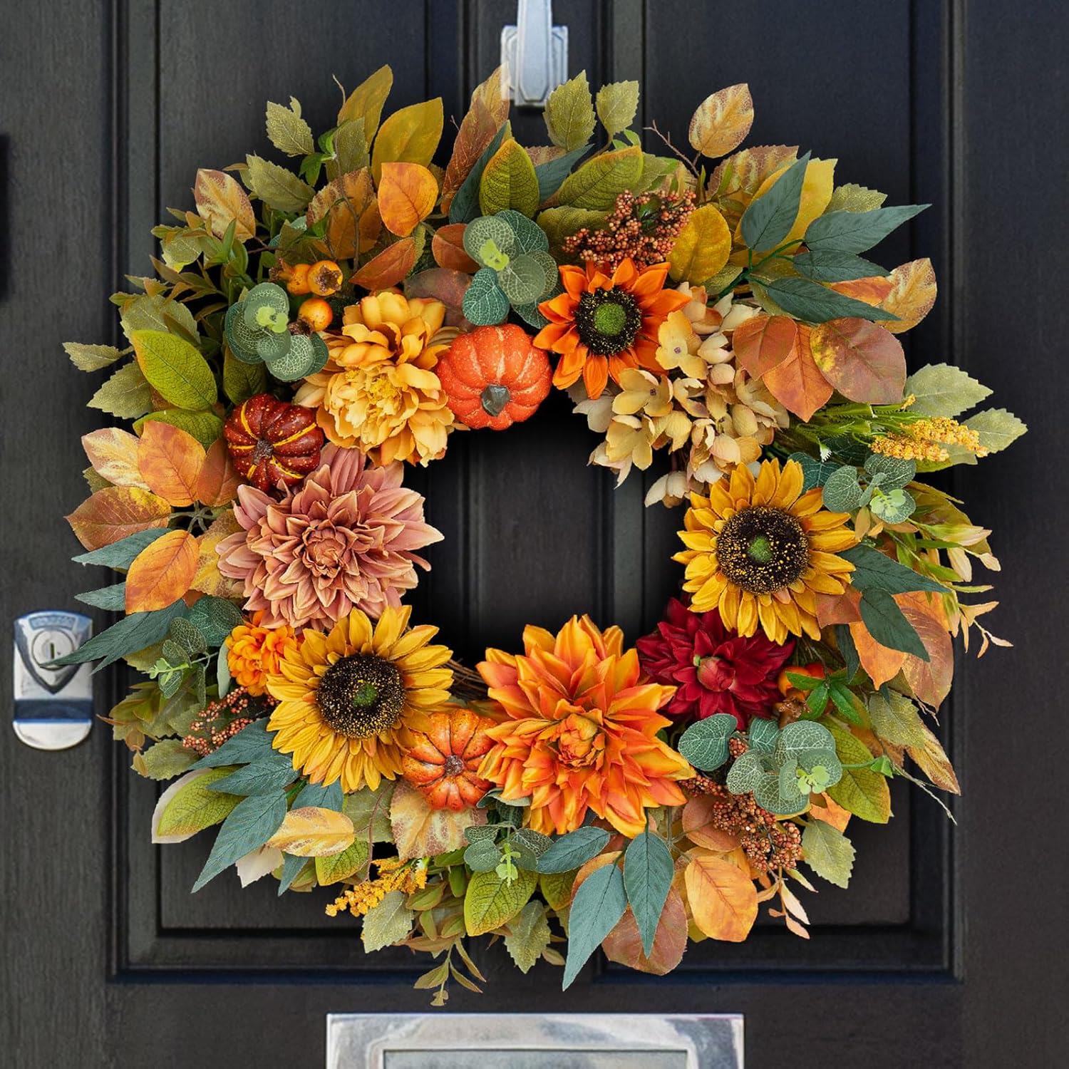 Autumn wreath with sunflowers, dahlias, and small pumpkins in orange and yellow tones on a dark door