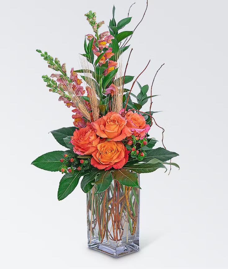 Orange roses in a clear glass vase with tall pink blooms