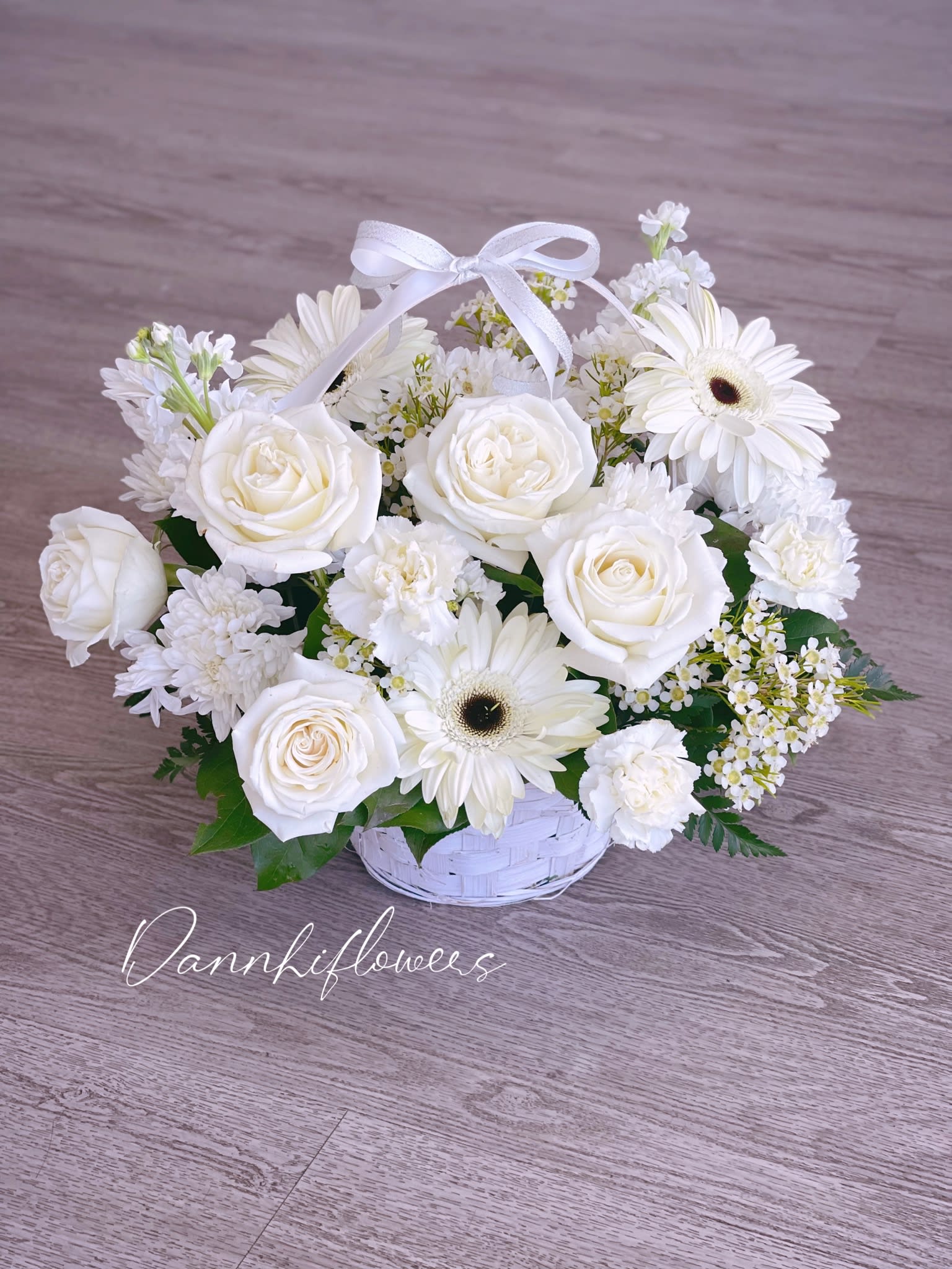 White roses and daisies arranged in a white basket with a ribbon bow