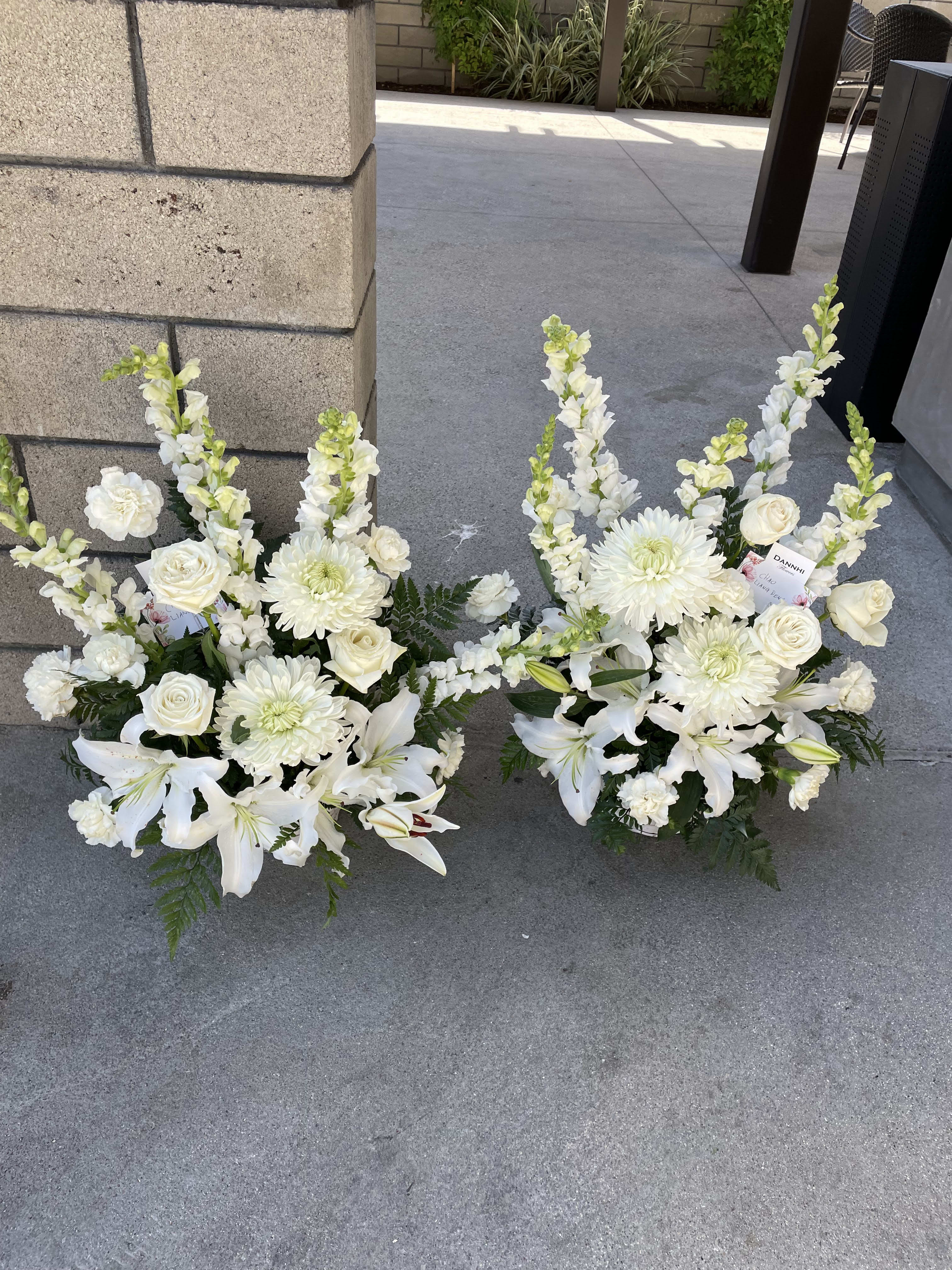 Two white floral arrangements with lilies, roses, and chrysanthemums on the ground.