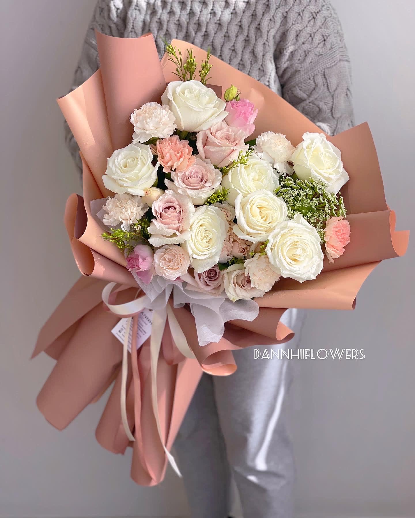 Bouquet of white and blush roses with carnations wrapped in peach paper