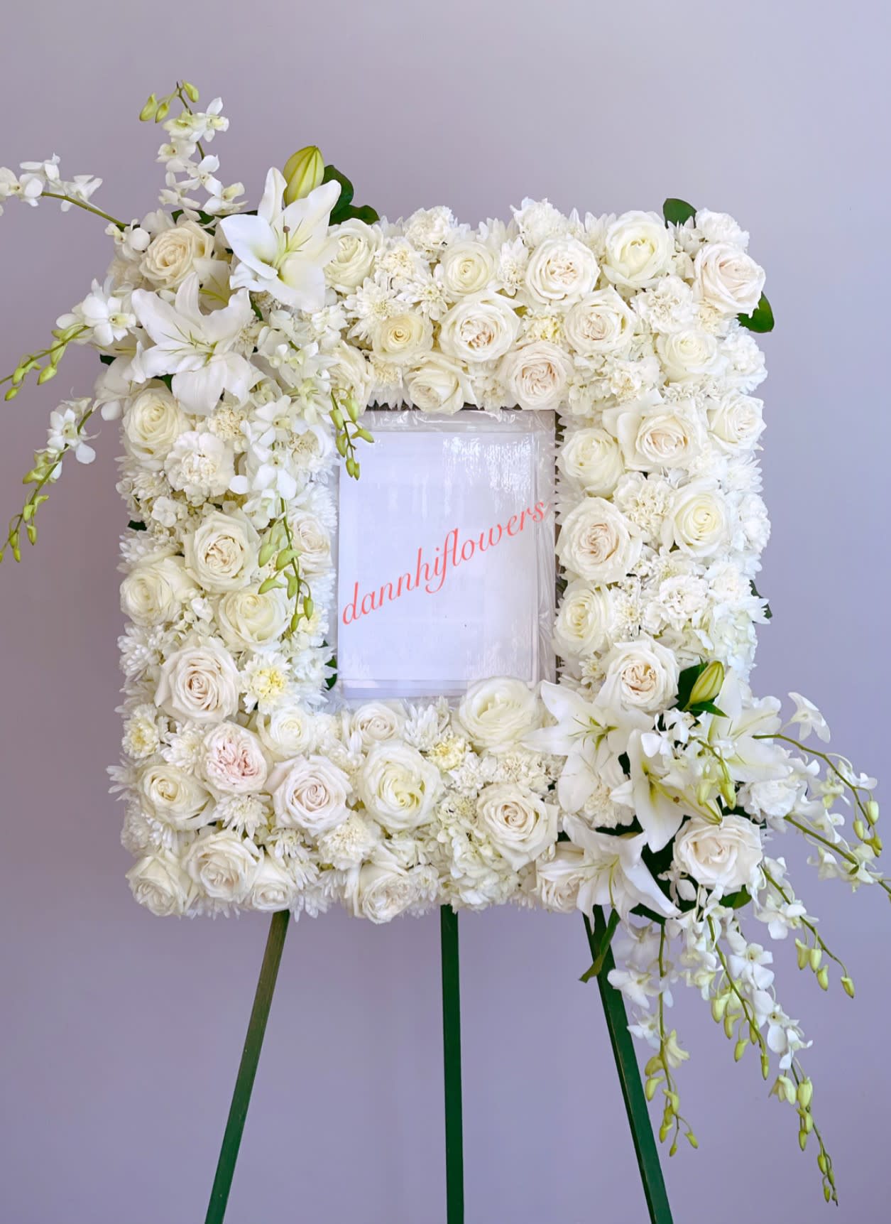 White floral wreath on an easel with roses and lilies