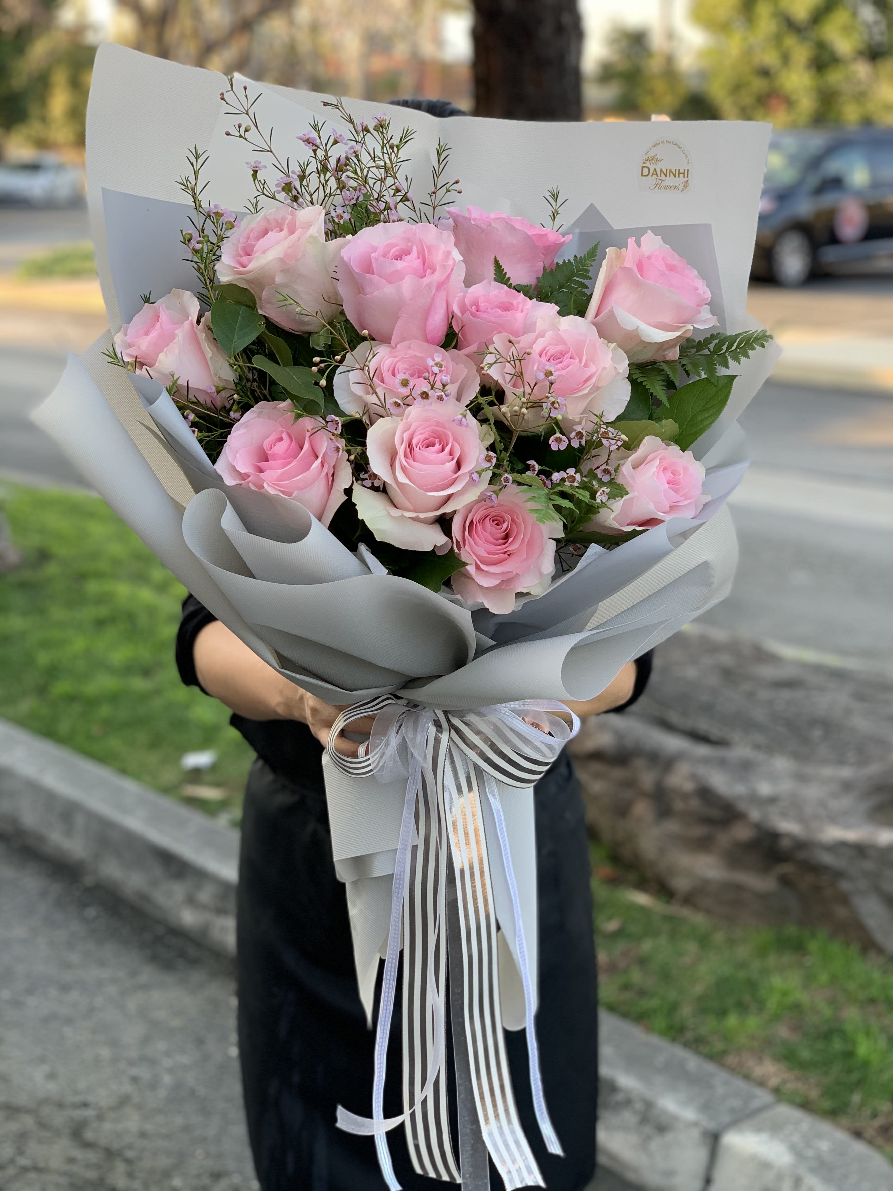 Handheld bouquet of pink roses wrapped in gray paper with ribbon