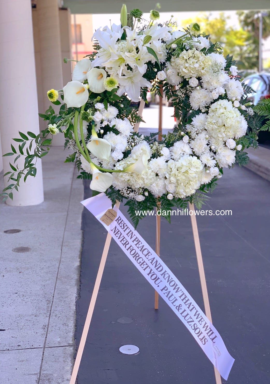 White funeral wreath on a wooden easel with a memorial ribbon