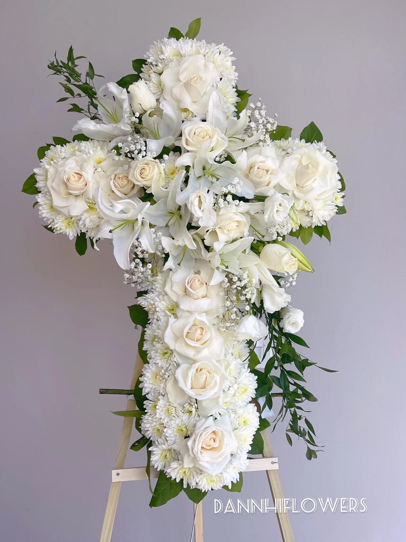 White floral cross arrangement on an easel with roses and lilies
