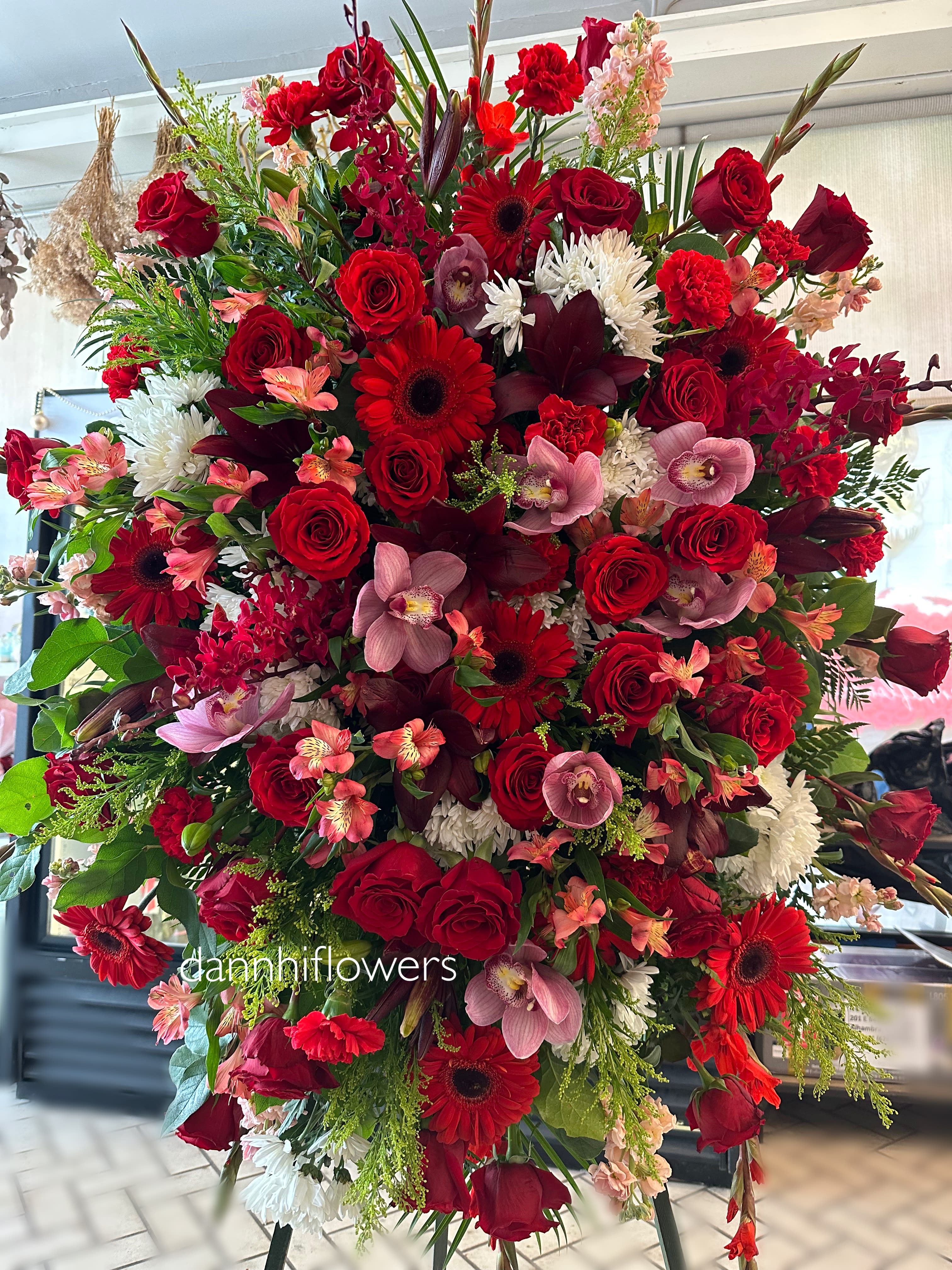 Large red floral standing spray with roses, gerberas, orchids, and white mums