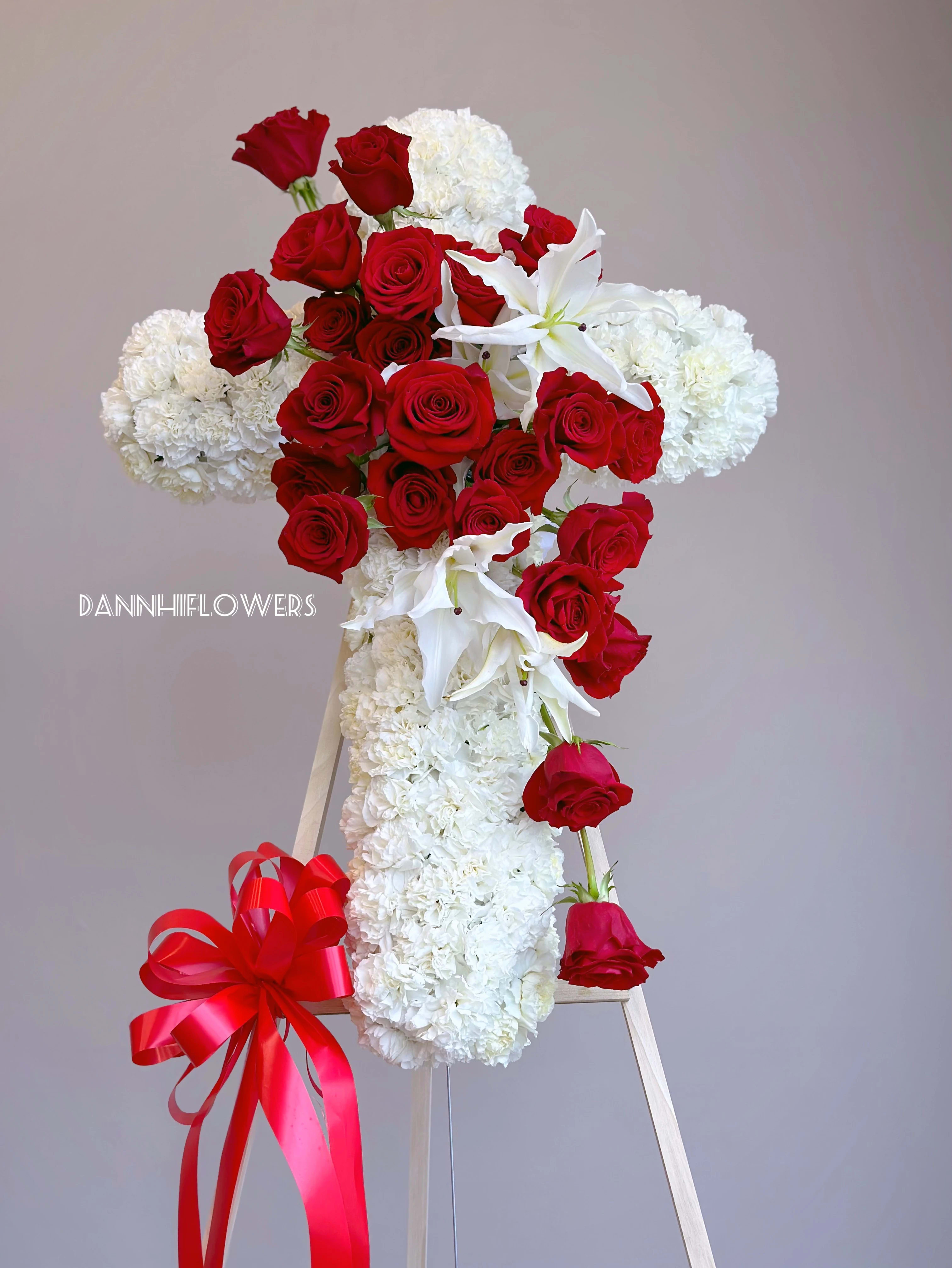 Red roses and white carnations arranged on a standing easel with a red ribbon bow