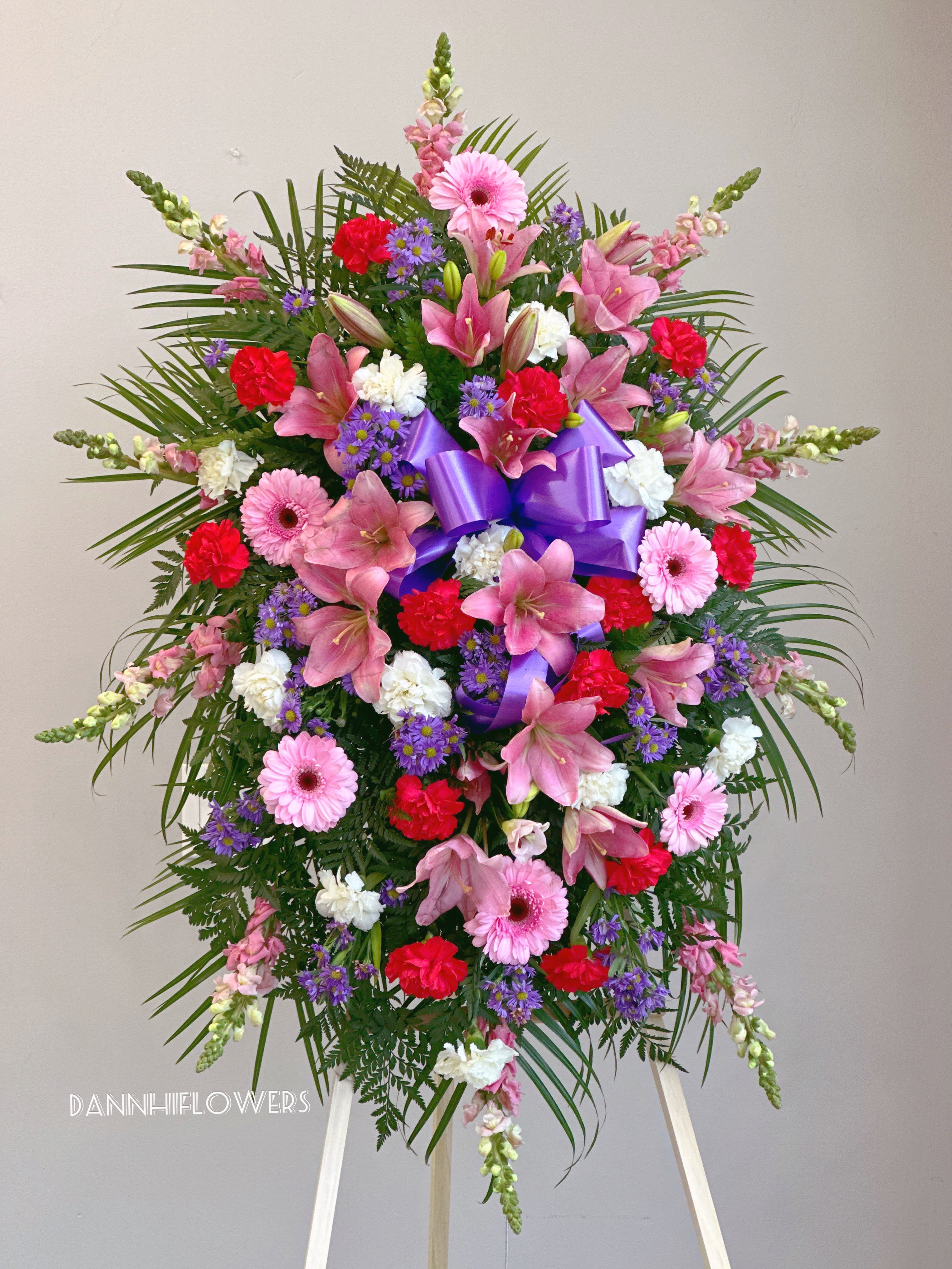 Standing floral spray with pink lilies, gerberas, carnations, and purple ribbon