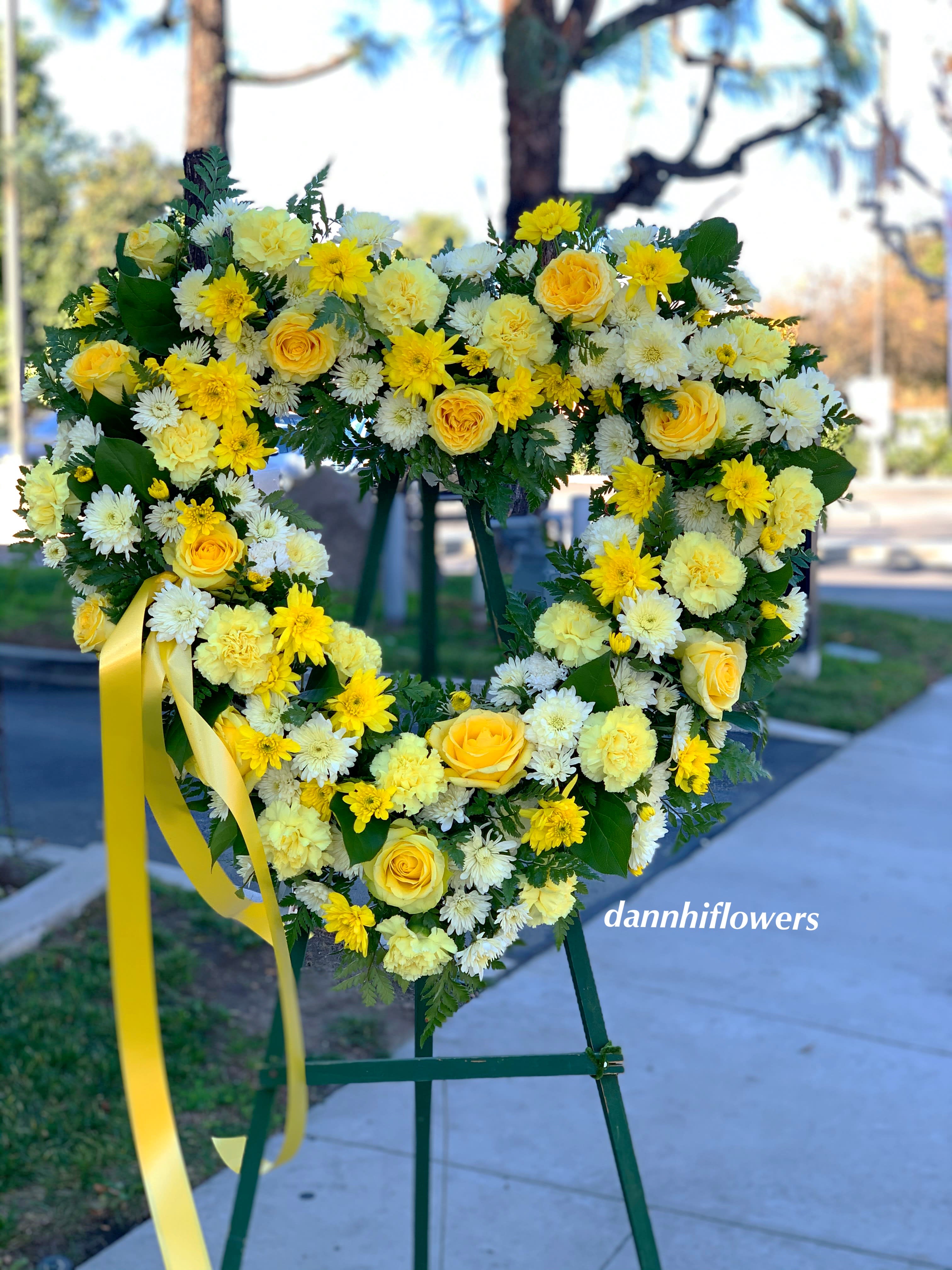 Heart-shaped yellow and white floral wreath on an easel with a ribbon