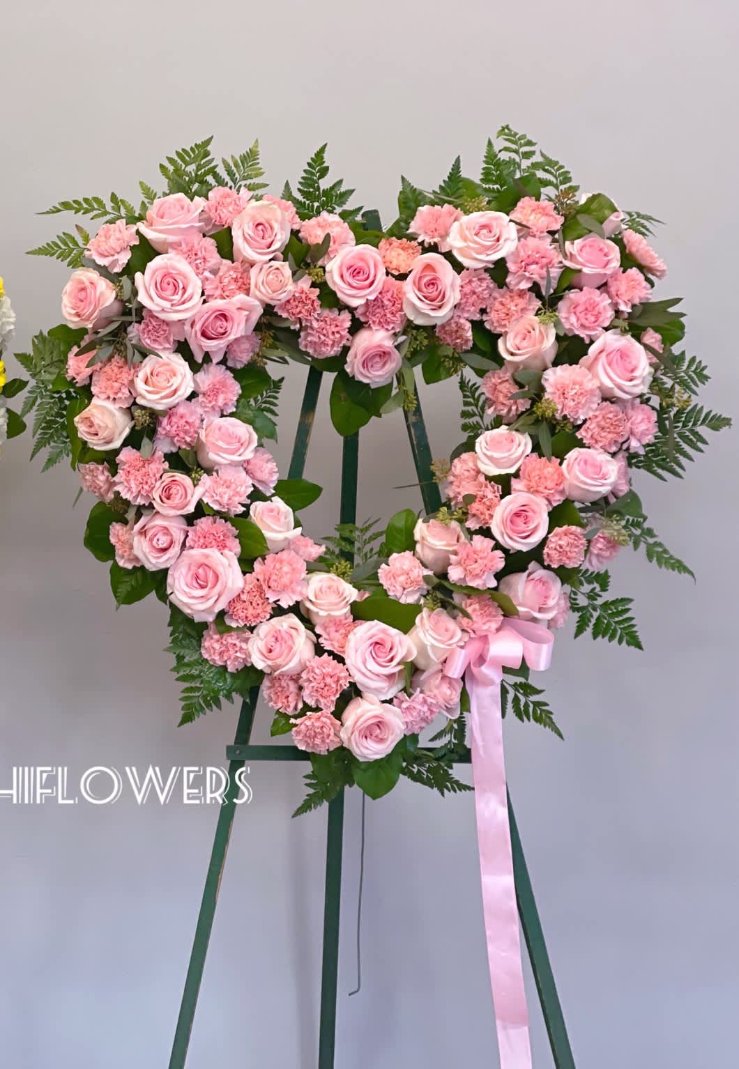 Heart-shaped pink rose and carnation wreath on a stand with a ribbon