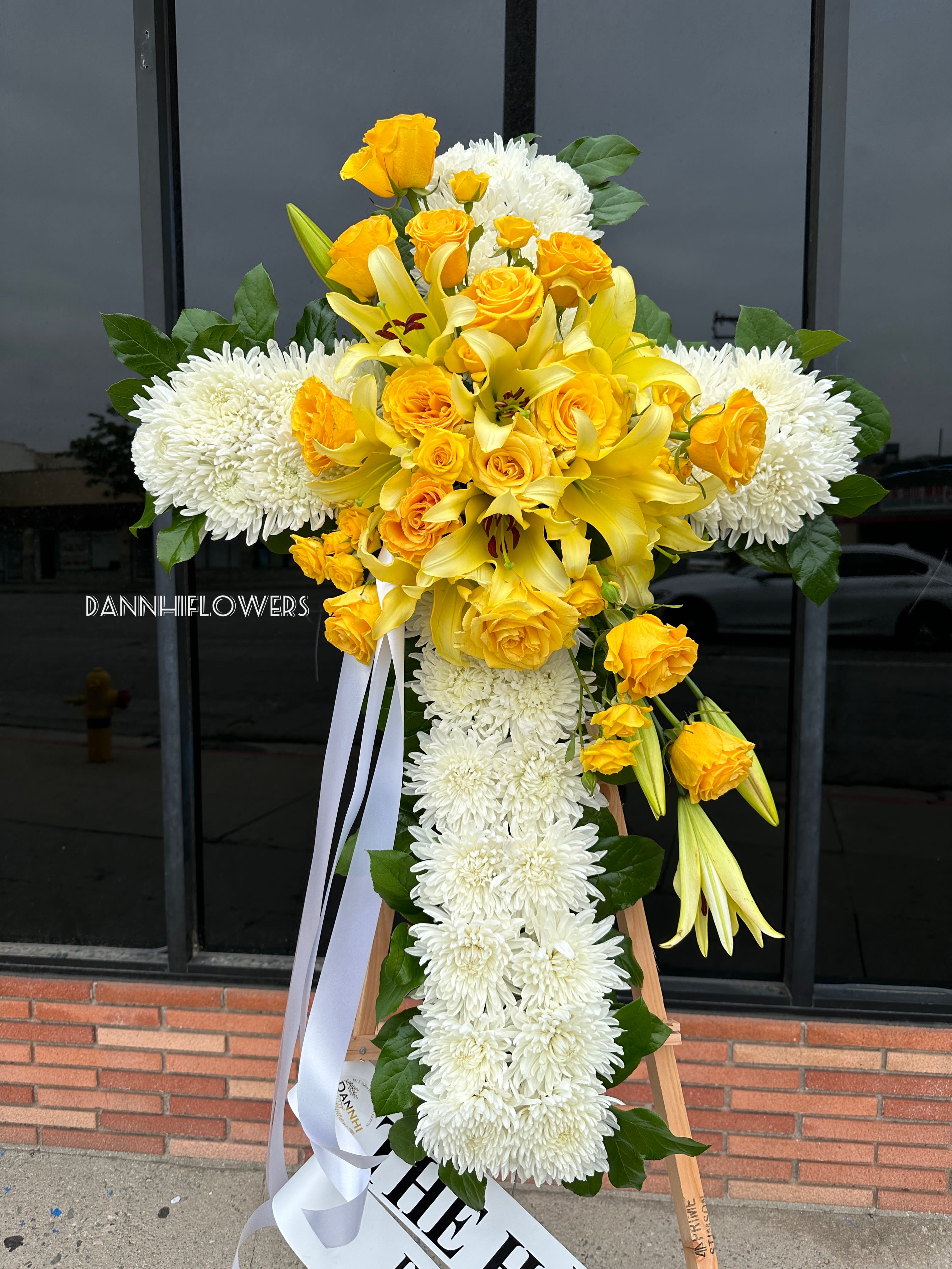 Yellow roses and lilies with white chrysanthemums on a standing cross arrangement
