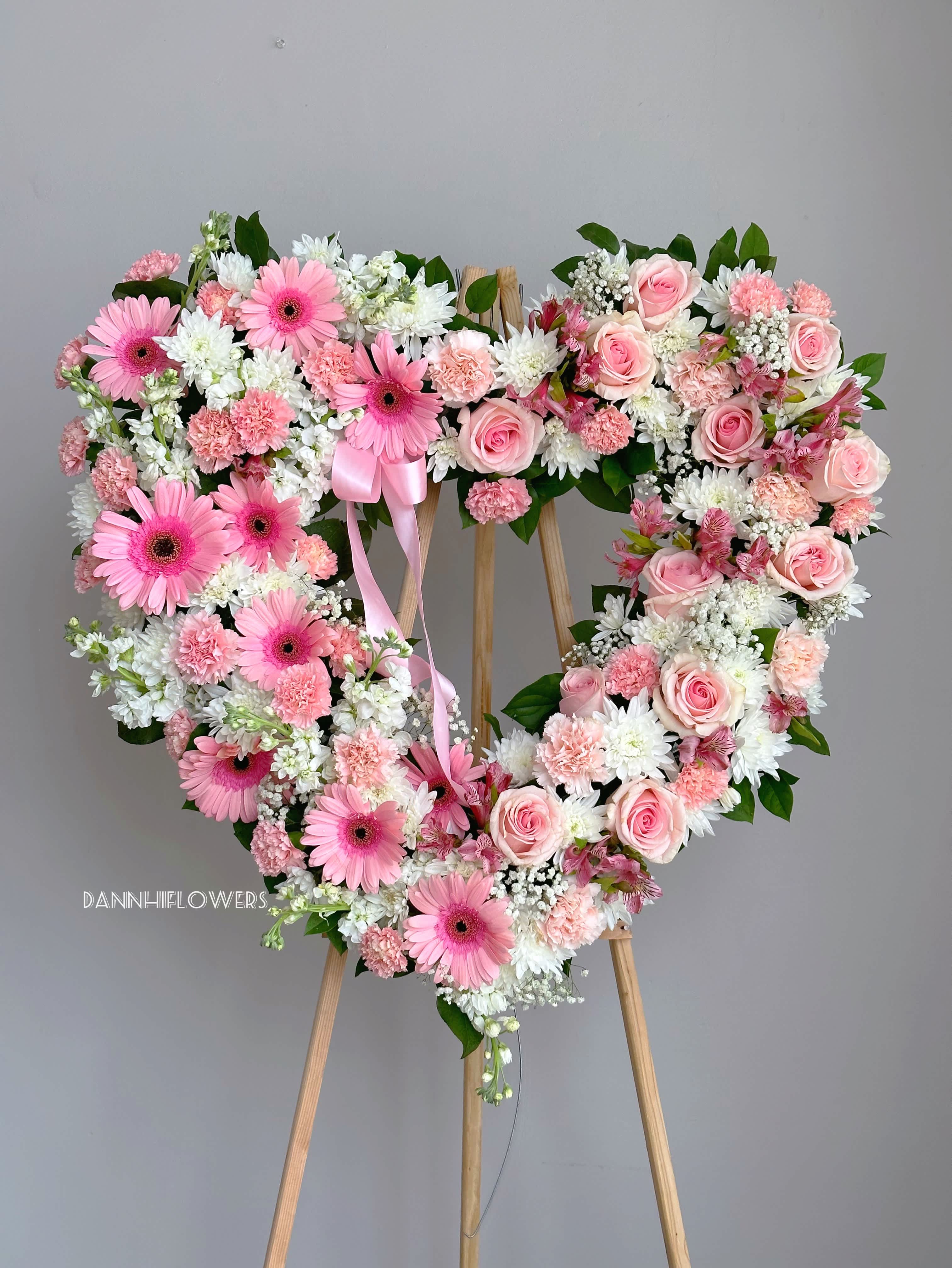 Heart-shaped floral wreath with pink roses and gerbera daisies on an easel