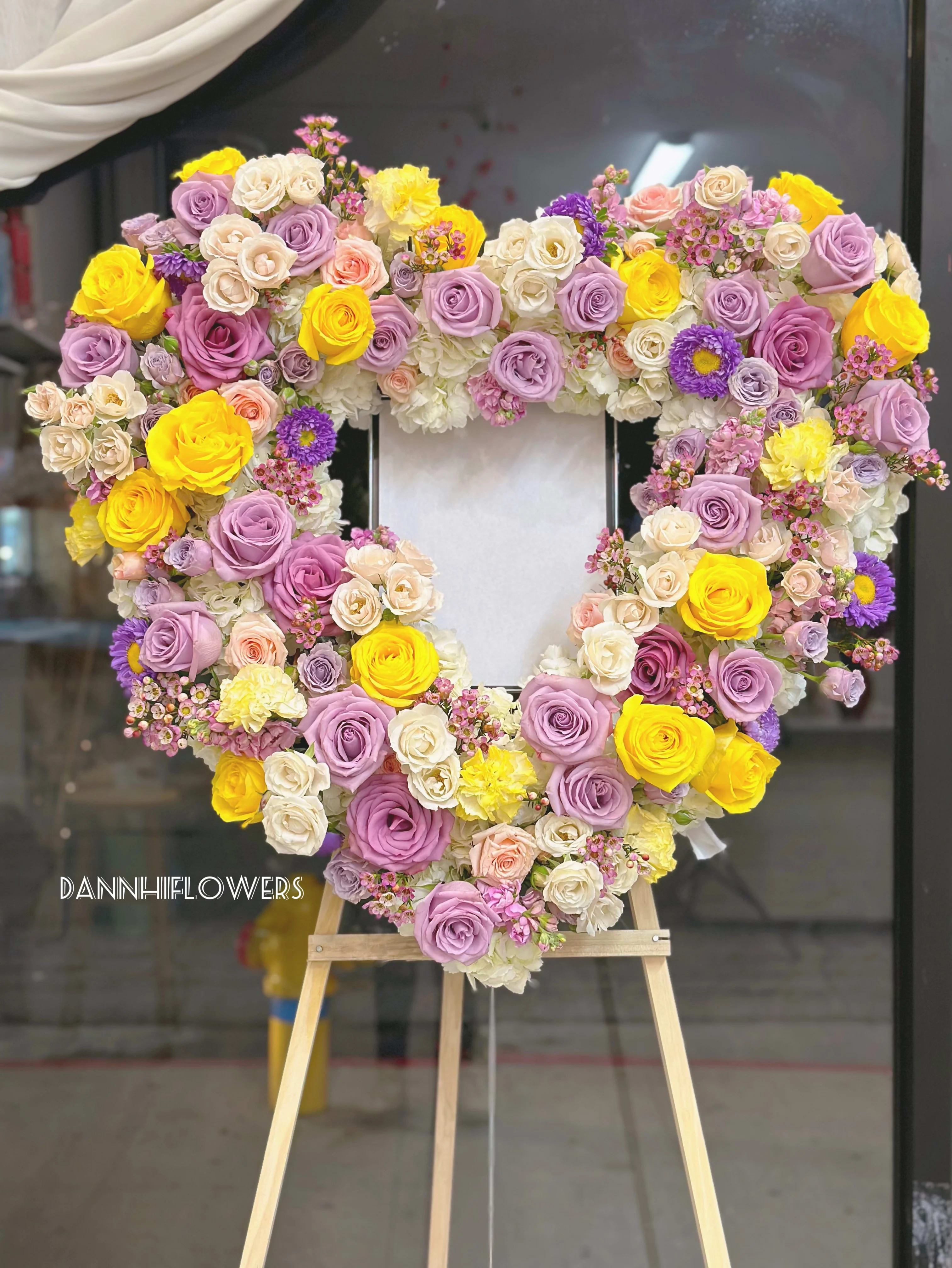 Heart-shaped floral wreath of roses in pink, lavender, white, and yellow