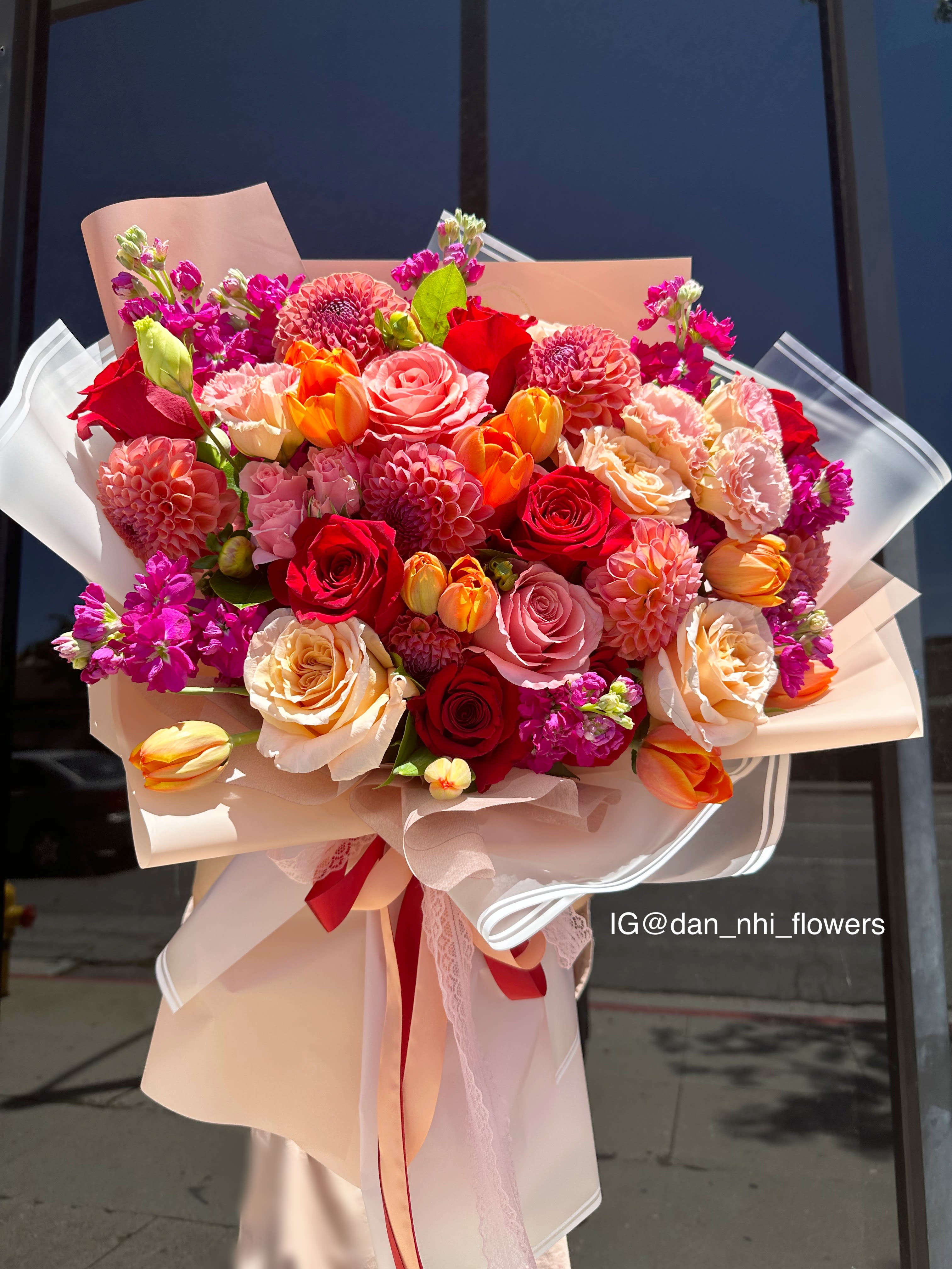 Large bouquet of red, pink, and peach flowers wrapped in blush paper
