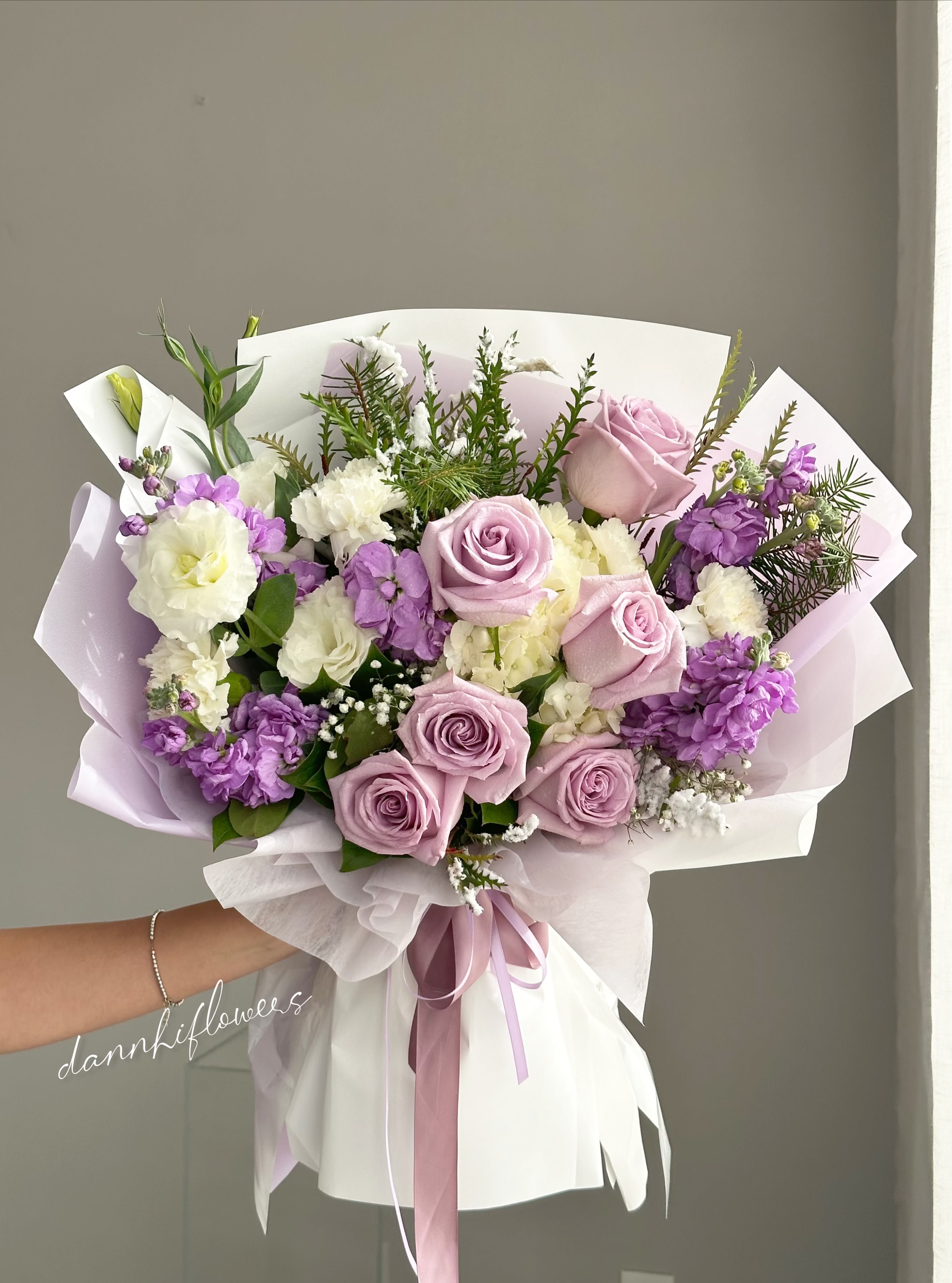 Hand-tied bouquet of lavender roses and purple-white blooms wrapped in pastel paper
