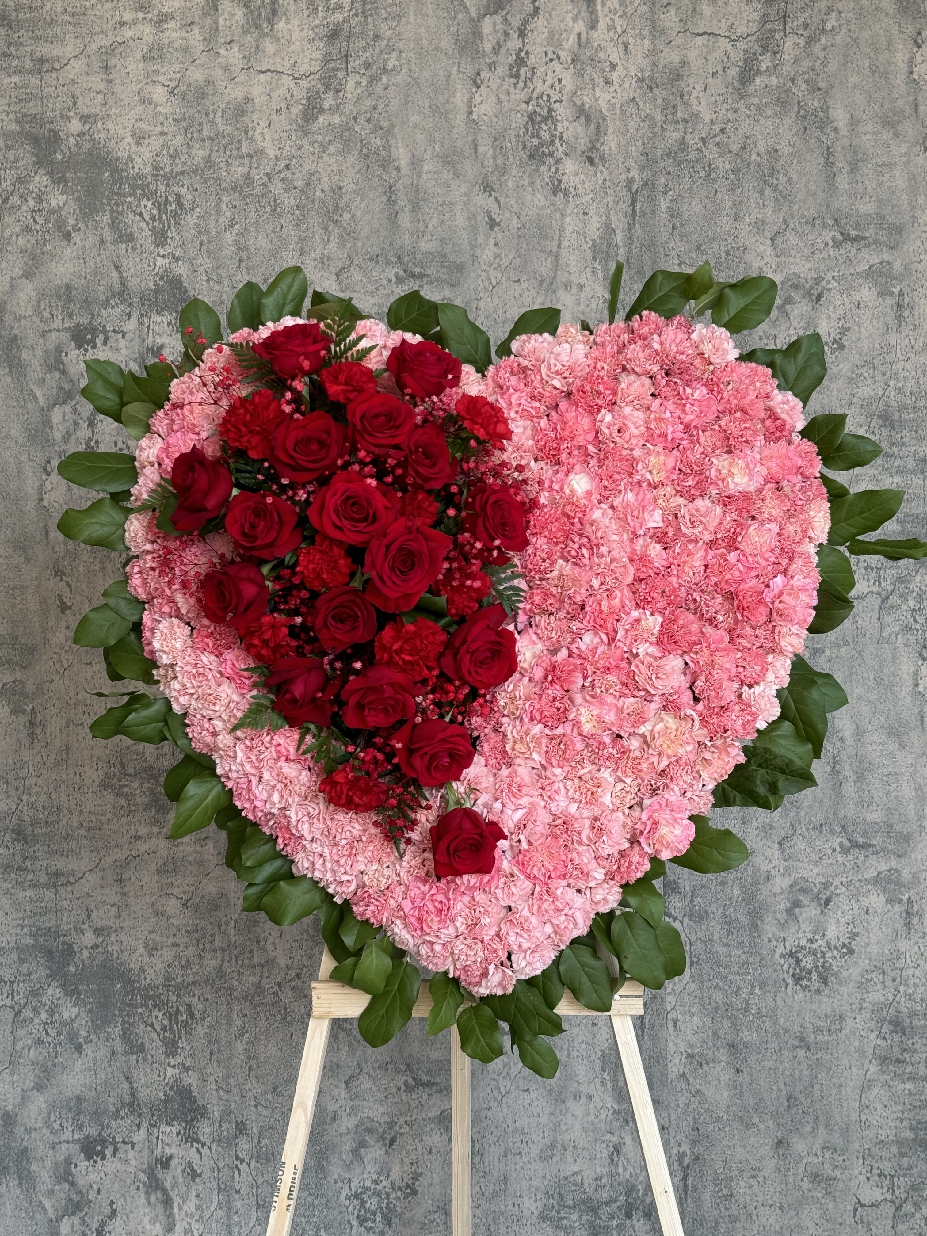 Heart-shaped floral tribute with red roses and pink carnations on an easel