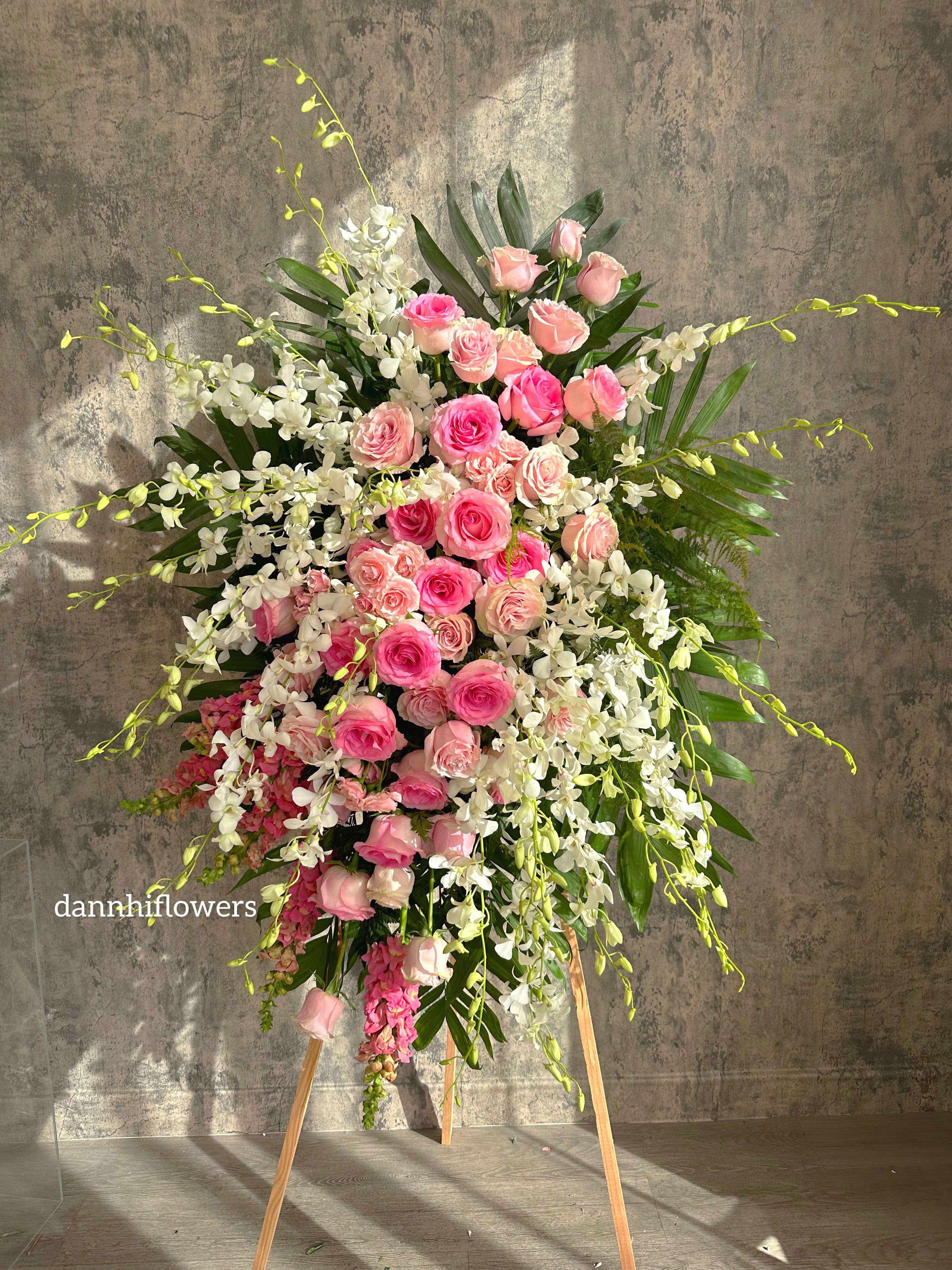 Tall standing arrangement of pink roses and white orchids on an easel