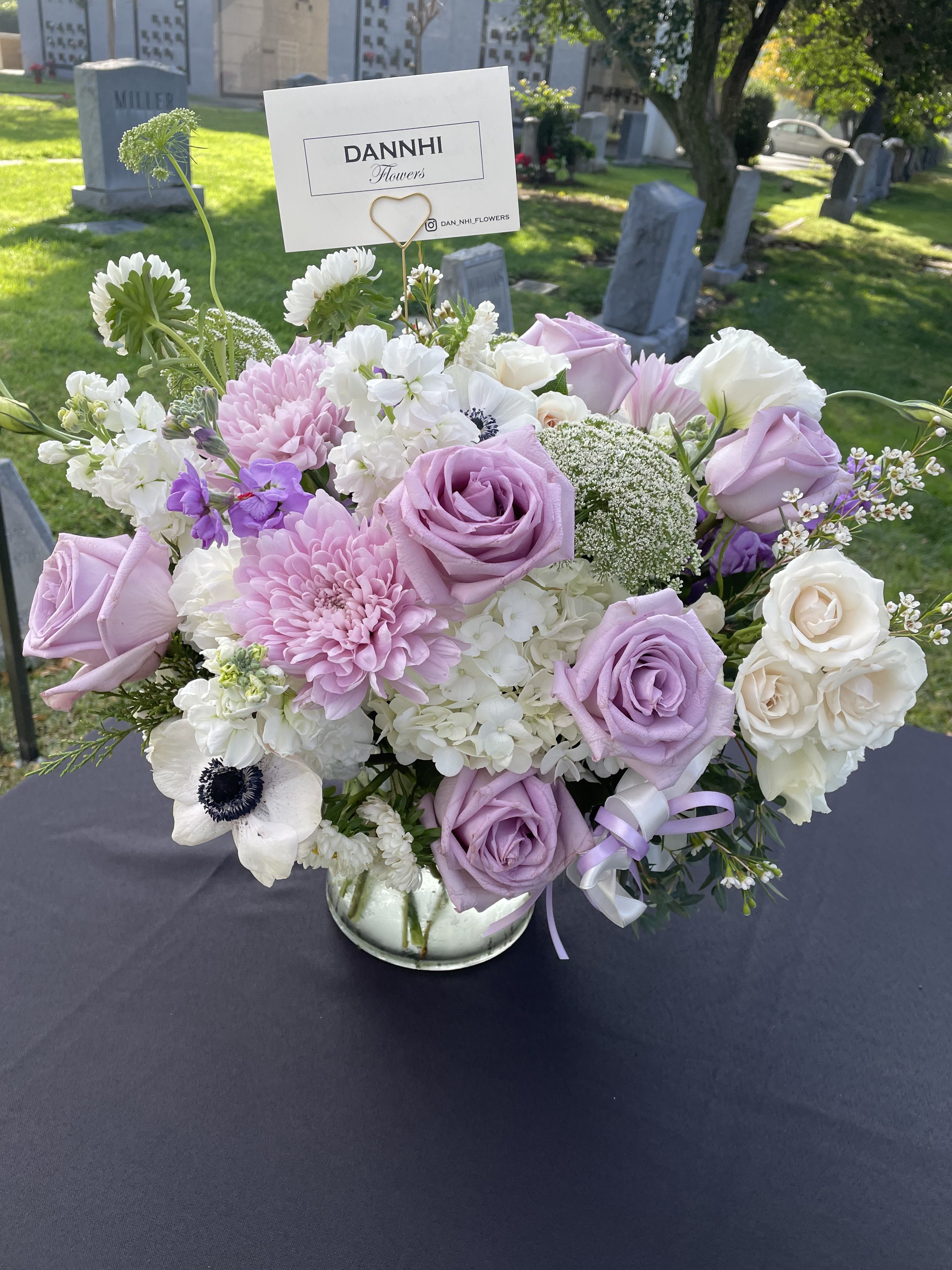 Lavender and white floral arrangement in a glass vase with a card pick