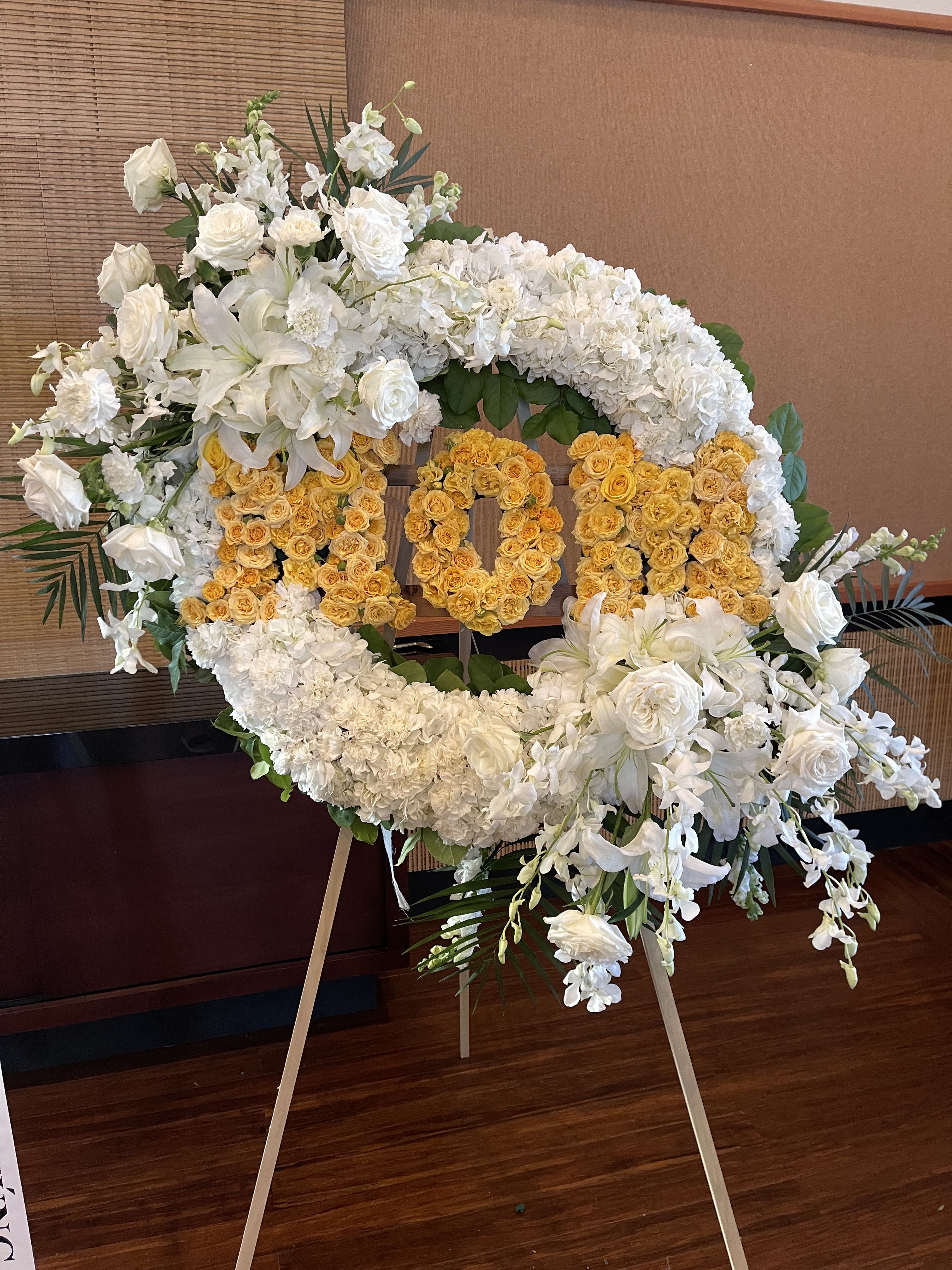 White and yellow floral wreath on an easel with large number 100