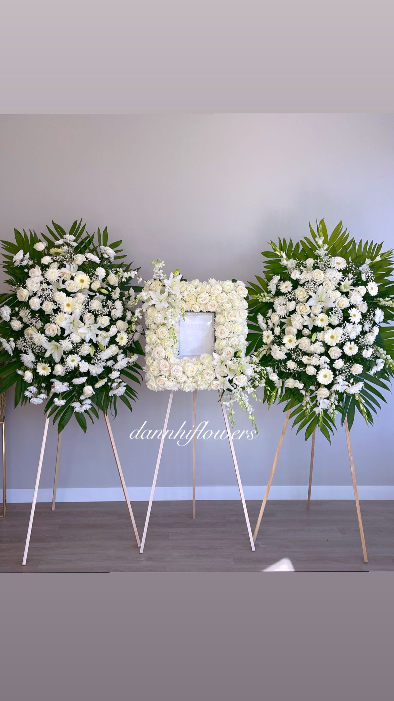 Three white floral funeral sprays on easels, with a rose frame in the center