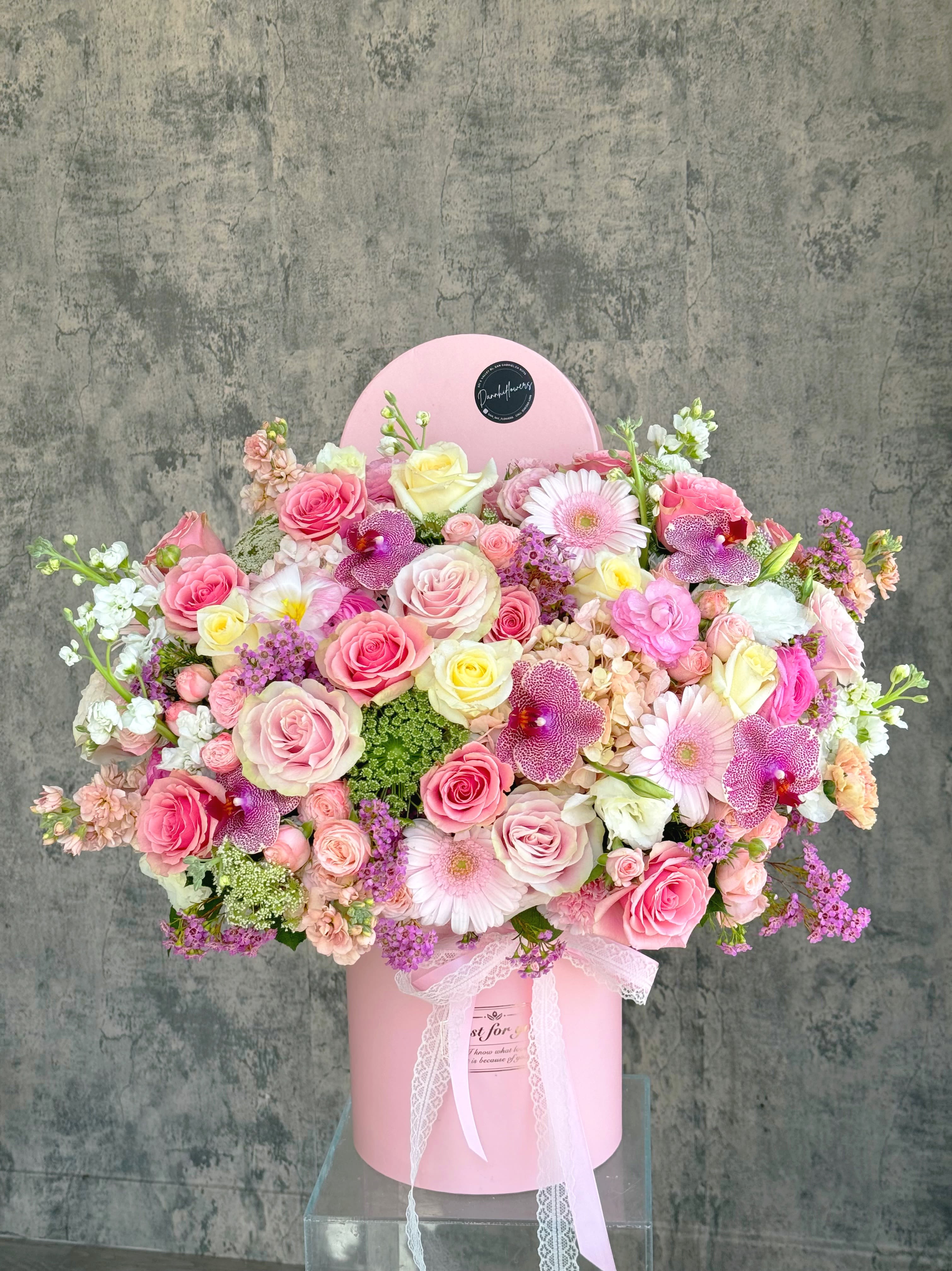 Large pink floral arrangement in a round pink box with a lace ribbon