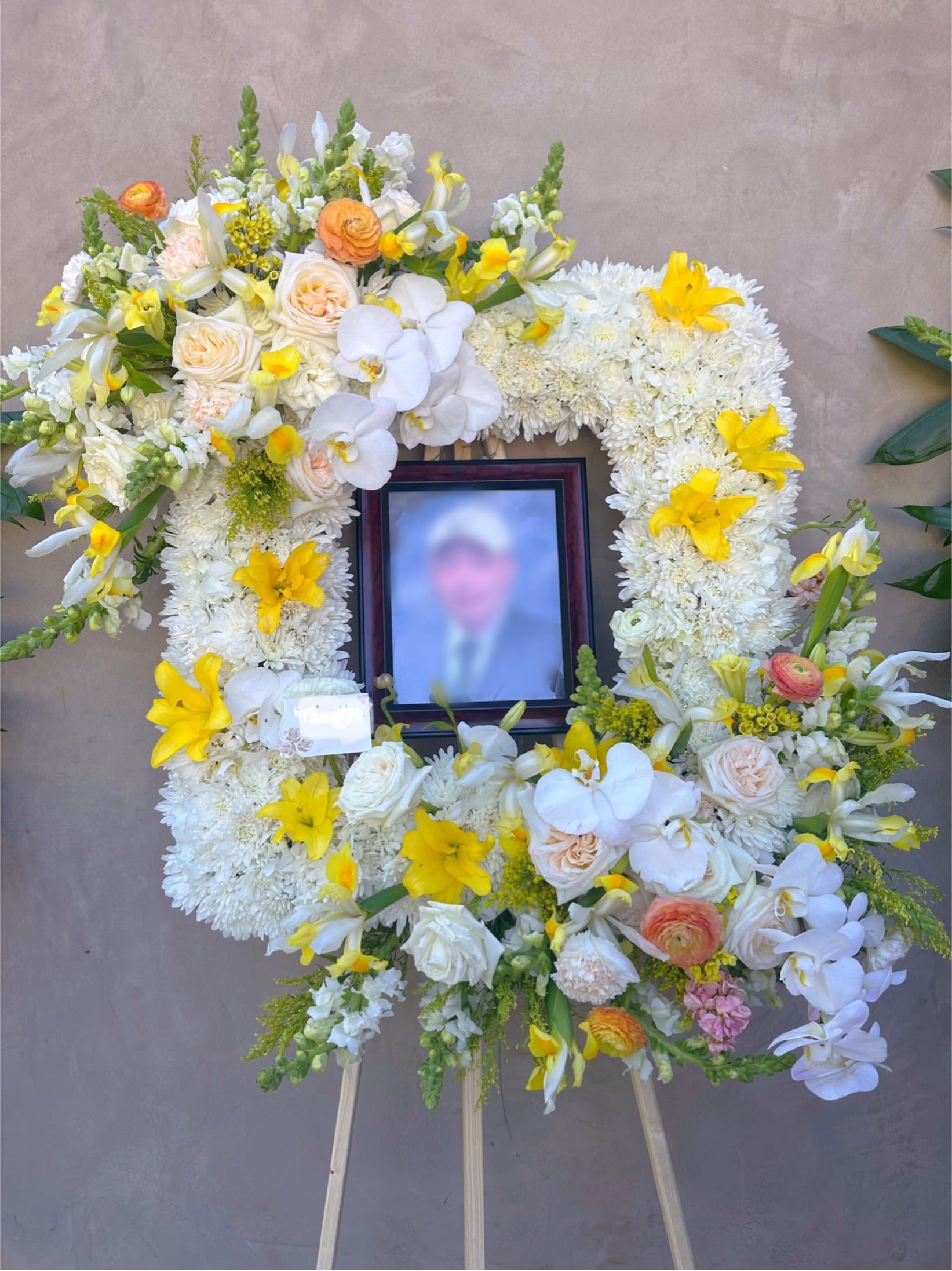 Large white and yellow floral funeral wreath on an easel with a framed photo in the center