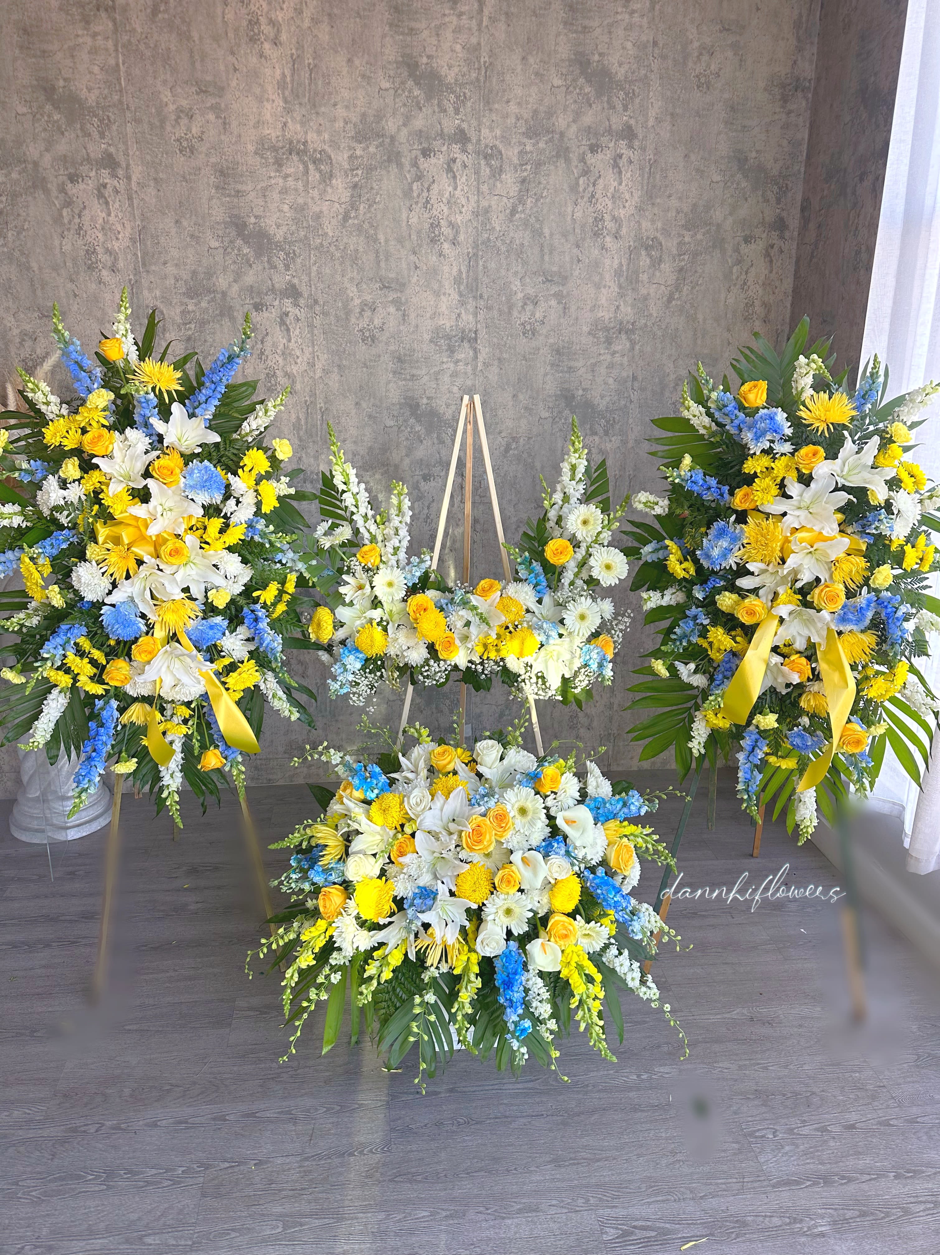 Three yellow, white, and blue floral funeral sprays with ribbons