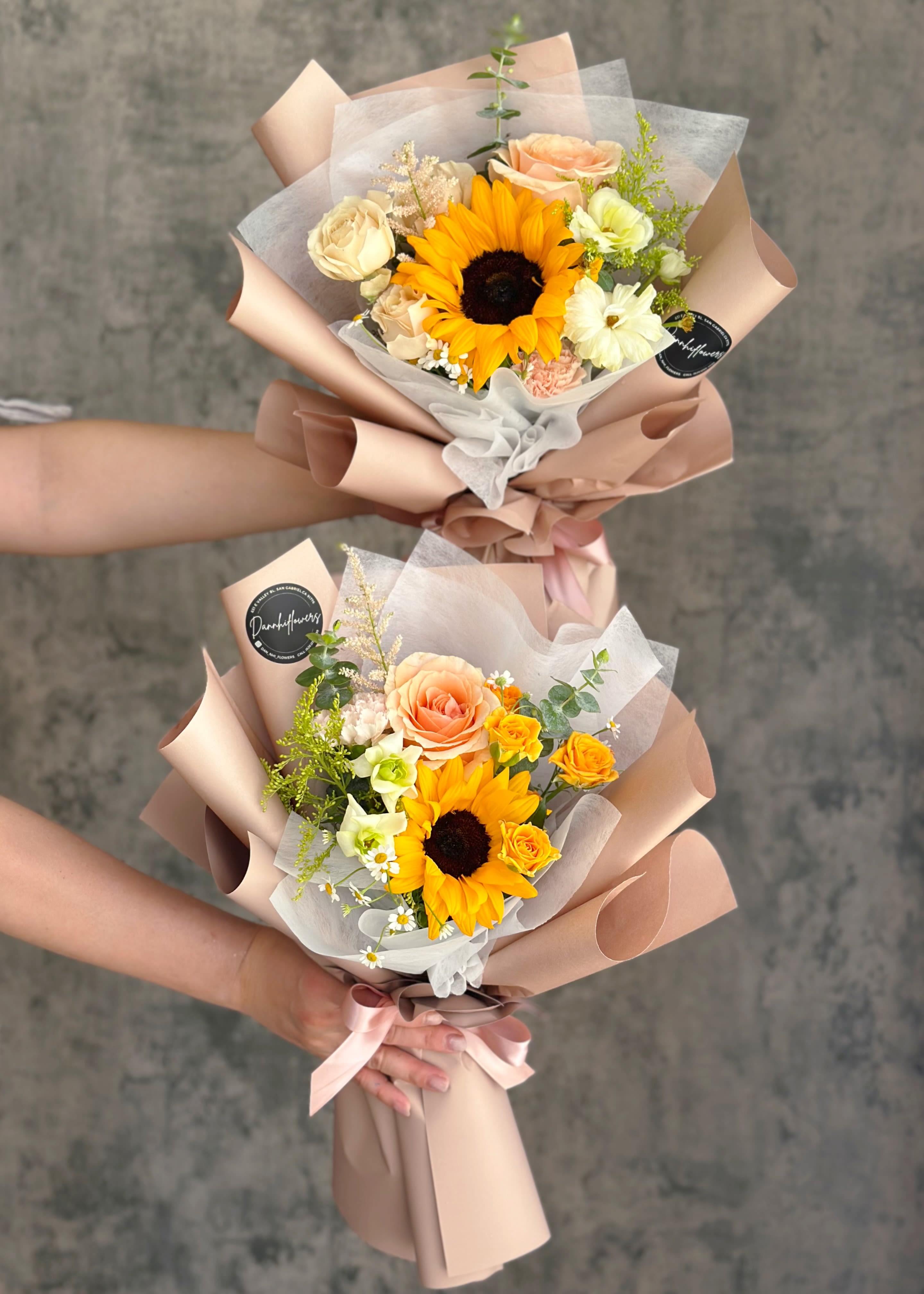 Two hand-tied bouquets with sunflowers and roses wrapped in blush paper