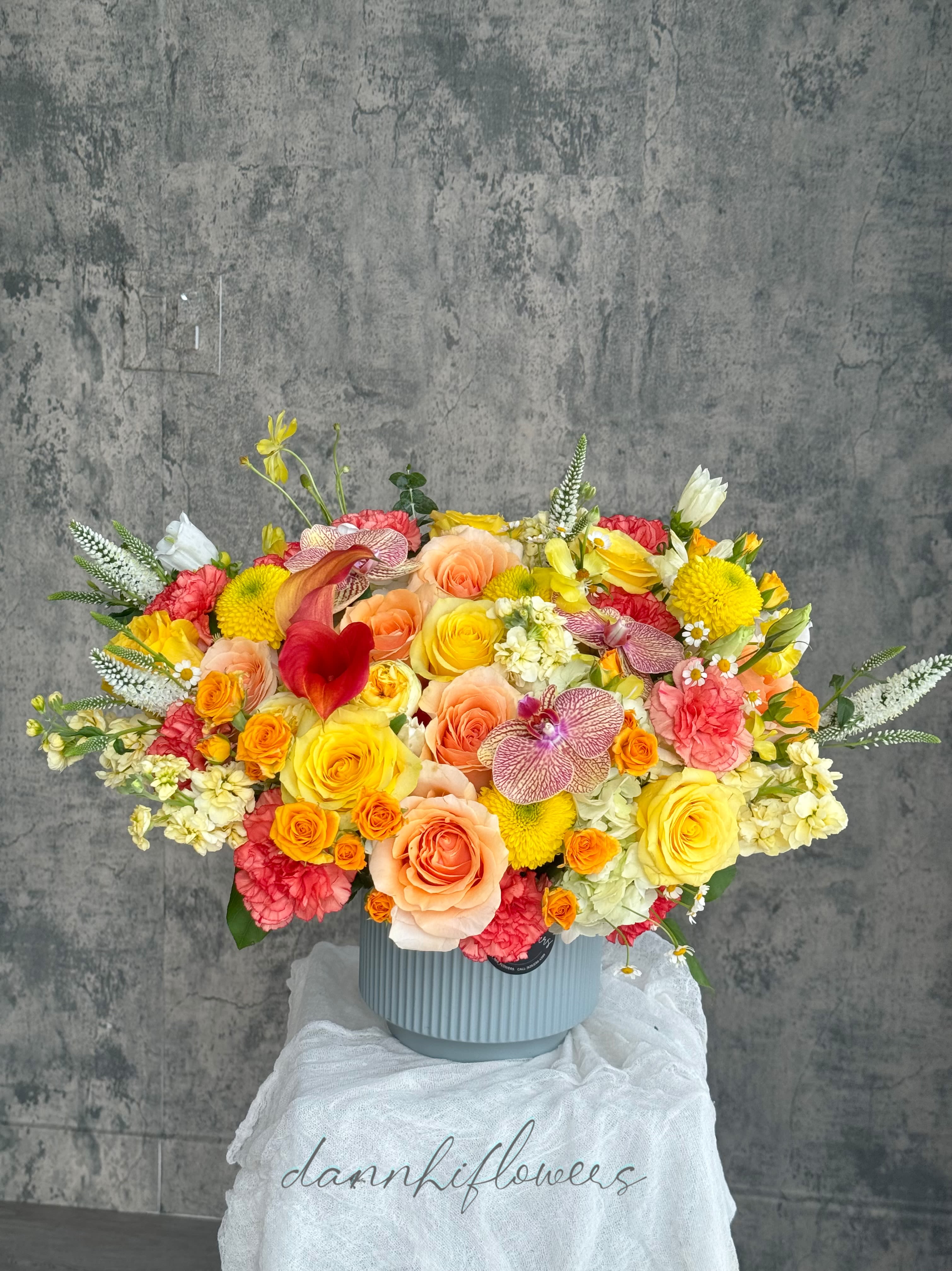 Large mixed bouquet in a ribbed blue vase with yellow, peach, pink, and white blooms